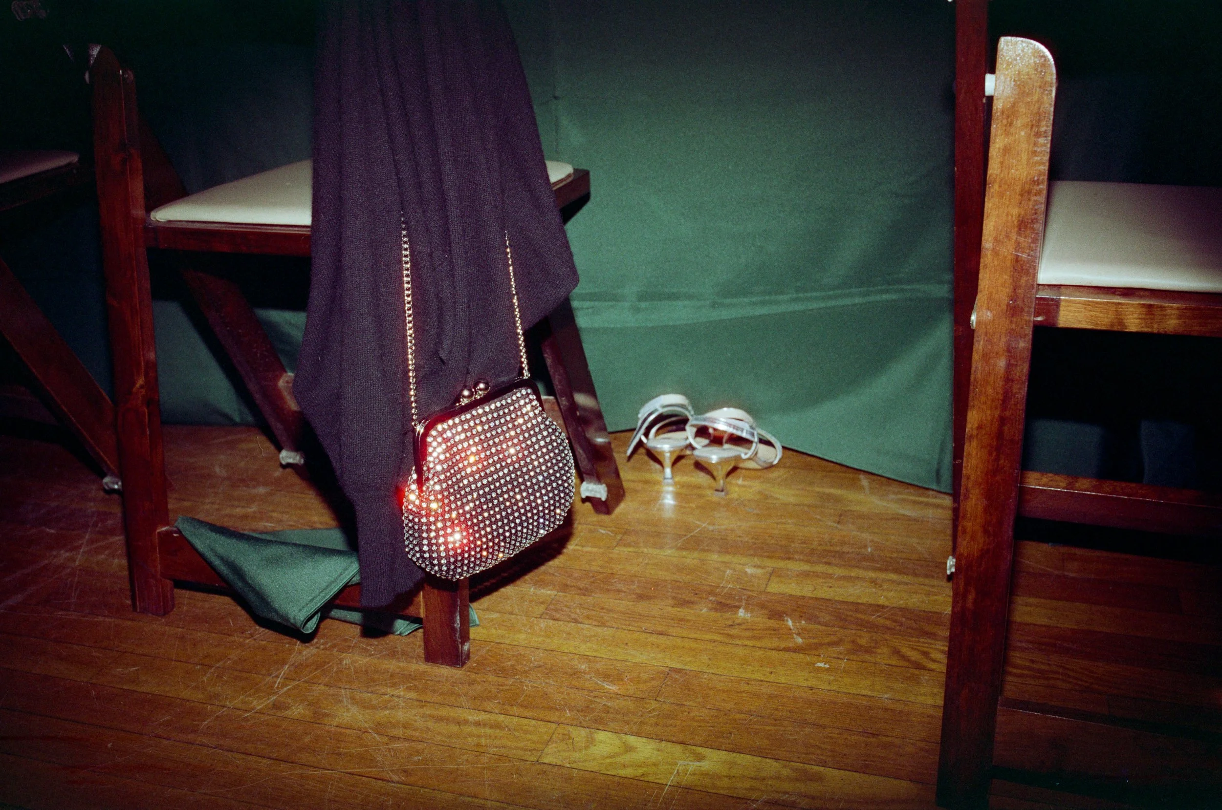 A bag hanging off of a chair with heels sitting next to it