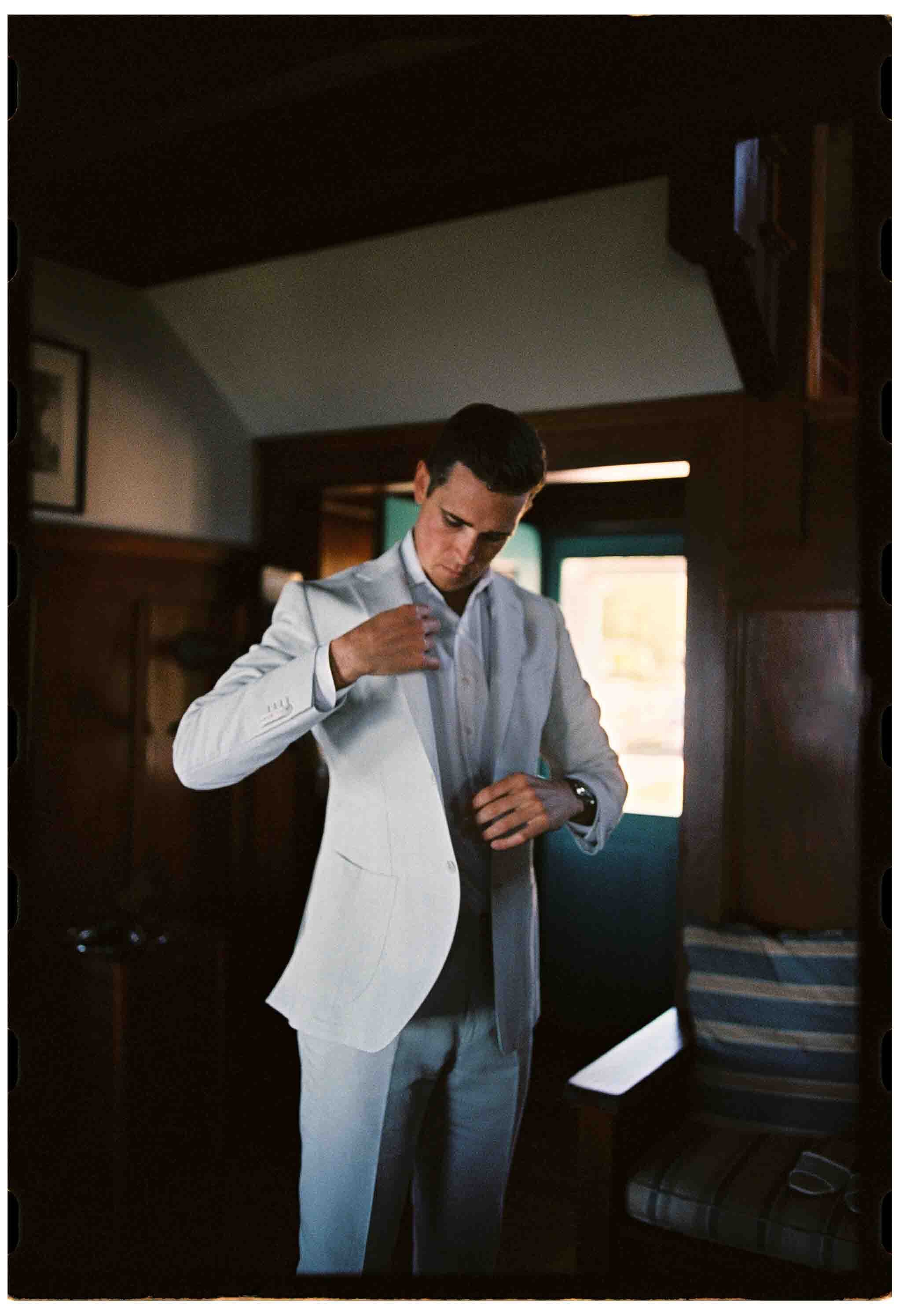 groom puts on suit jacket before his wedding ceremony