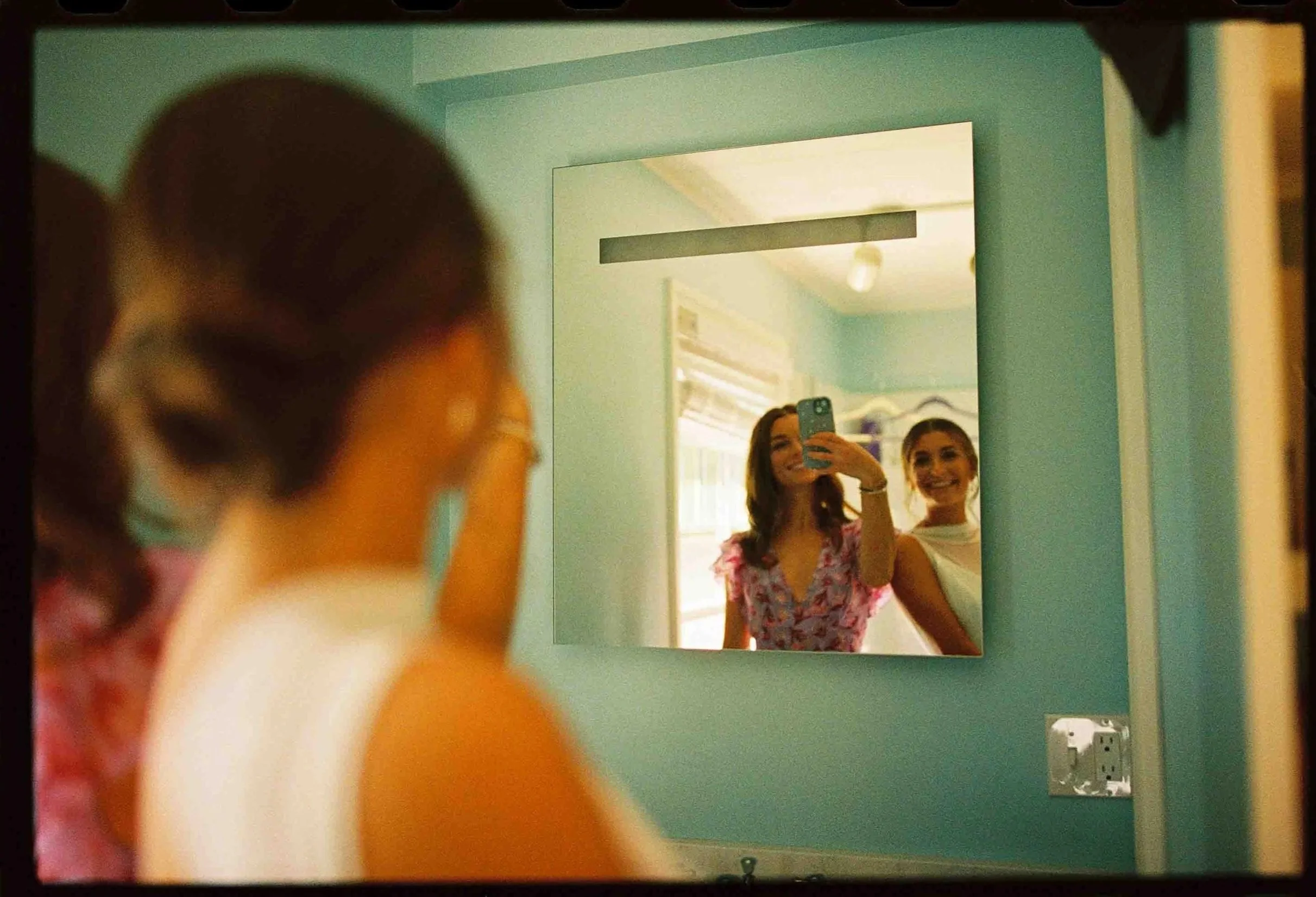 A newlywed and a guest taking a selfie in a mirror