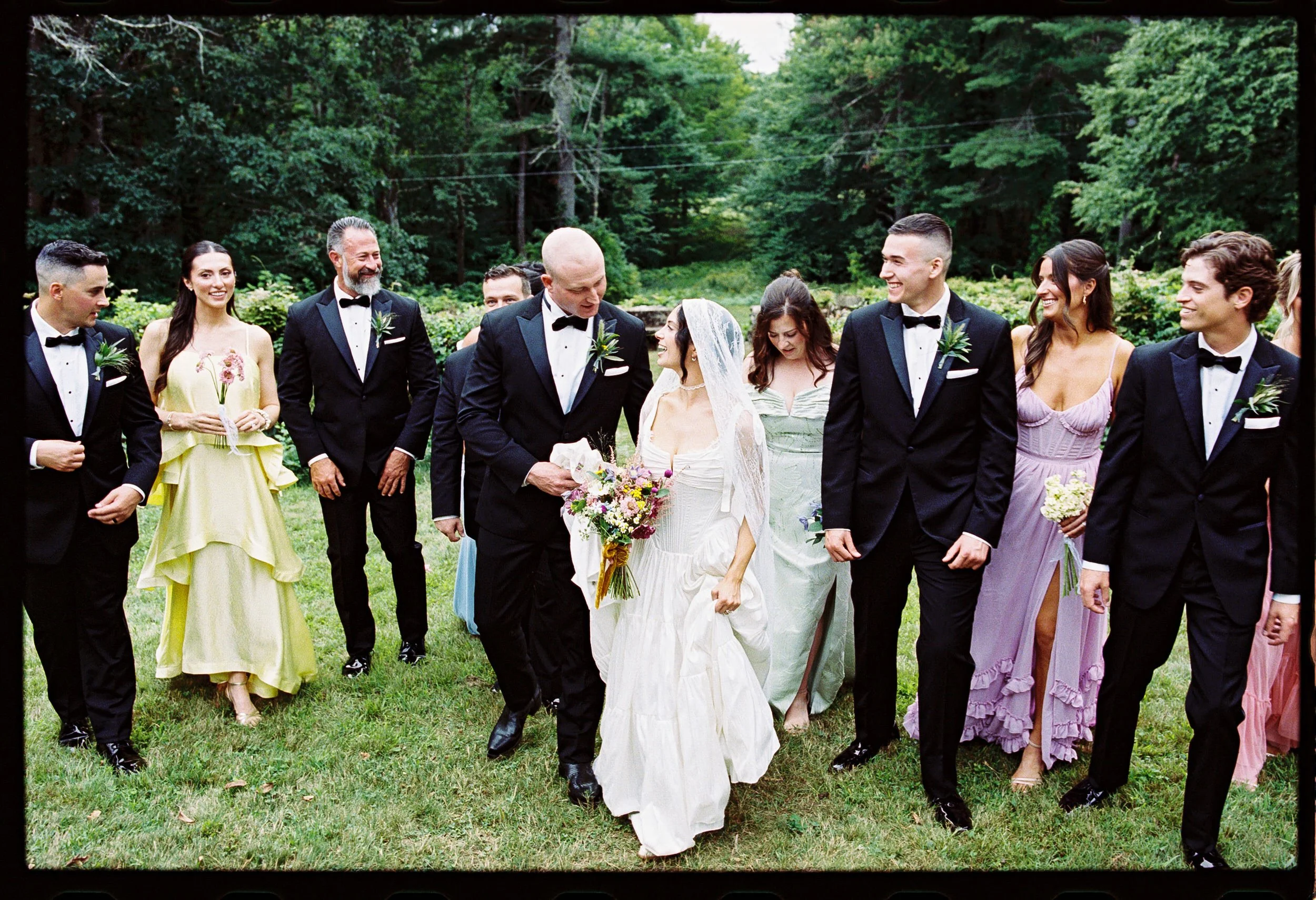 Newlyweds smiling at each other with their wedding parties around them