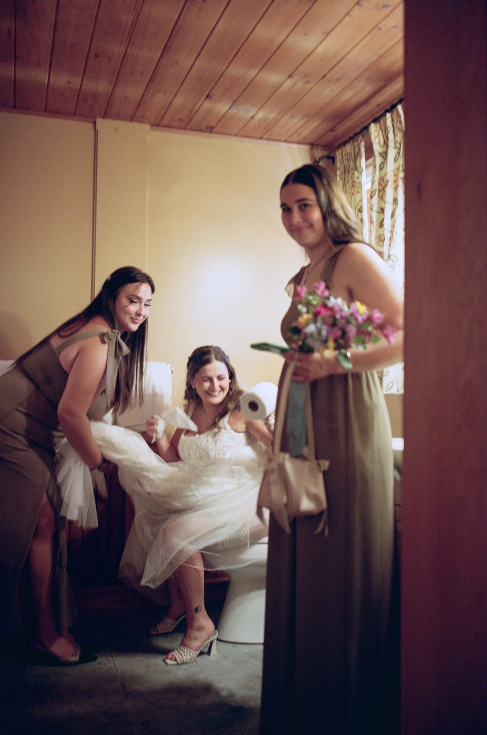 A newlywed in a wedding dress sitting in the bathroom with two of their wedding party