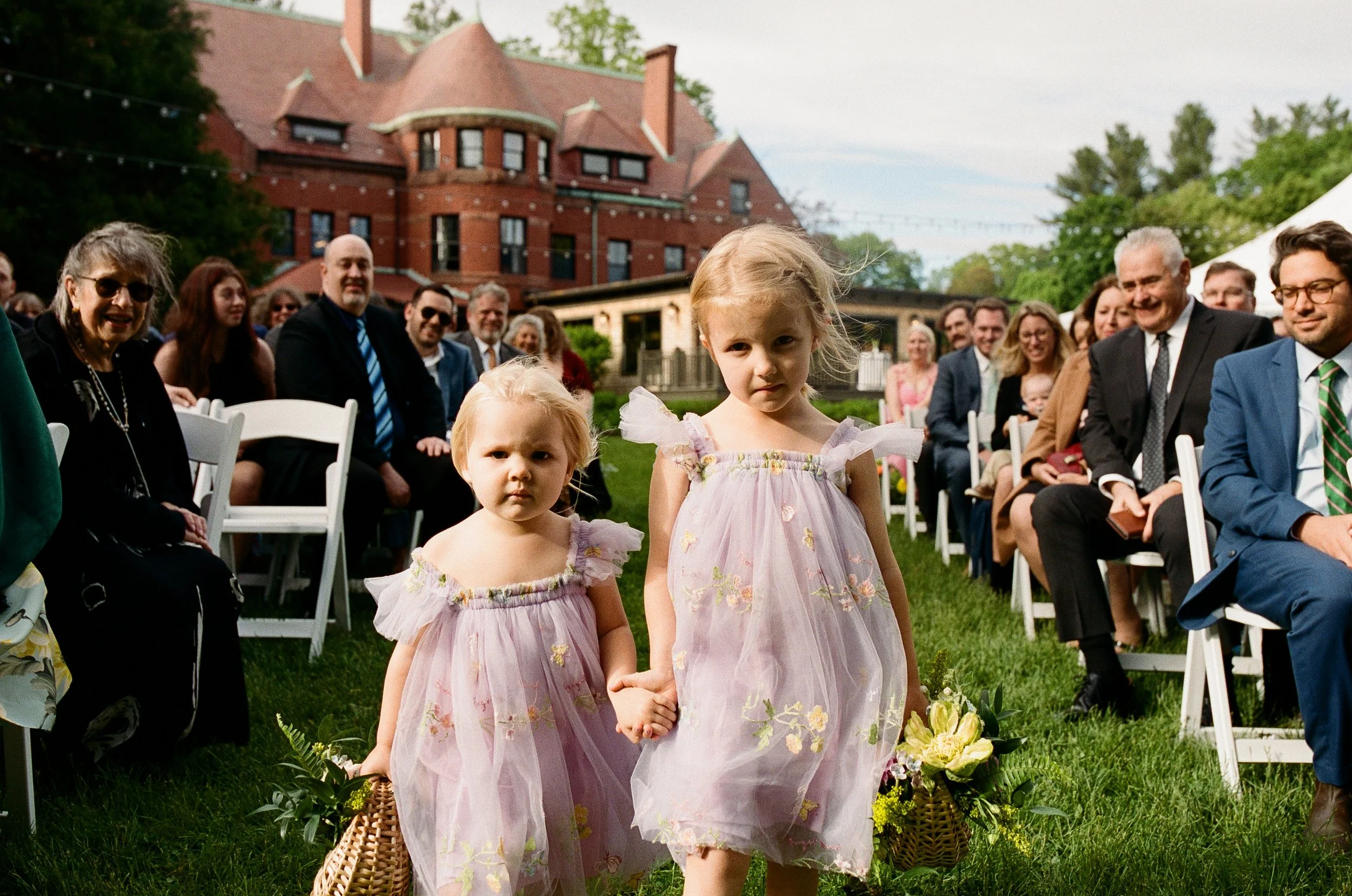 flowergirls hold hands and stare directly into camera walking down the aisle at at wedding stevens osgood estate