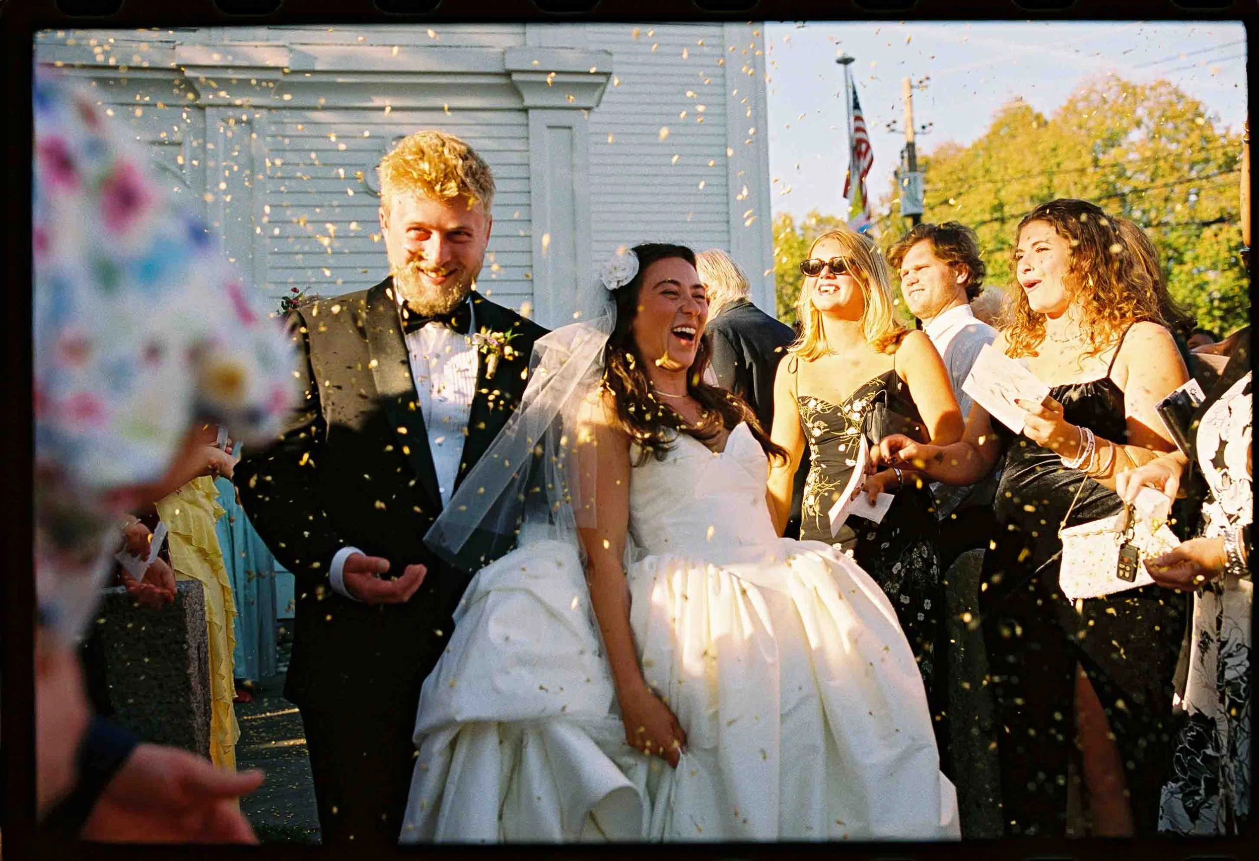Newlyweds laughing as they walk through their wedding guests who are throwing confetti