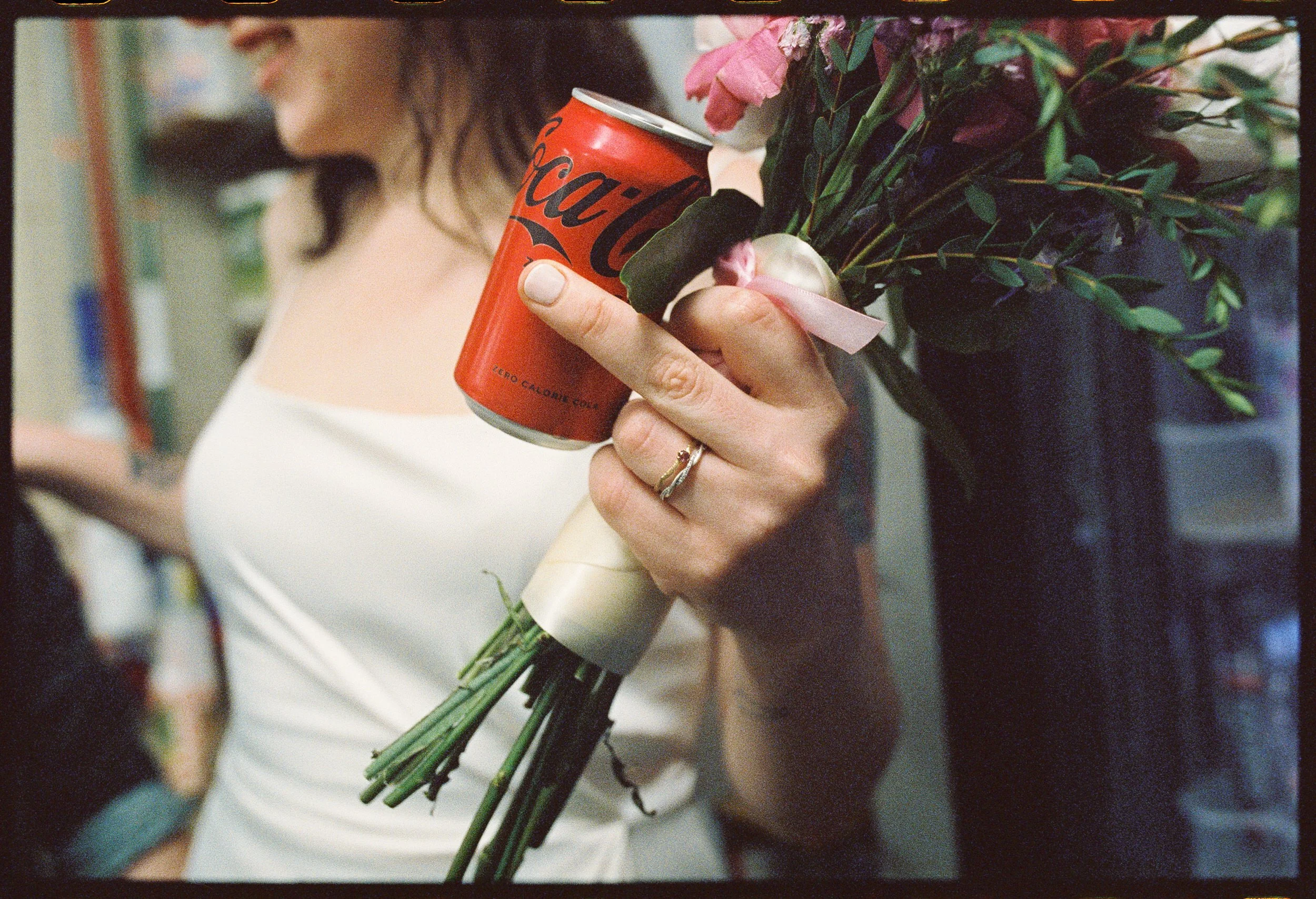 A newlywed holding up a middle finger while also holding a bouquet and a can of coke zero
