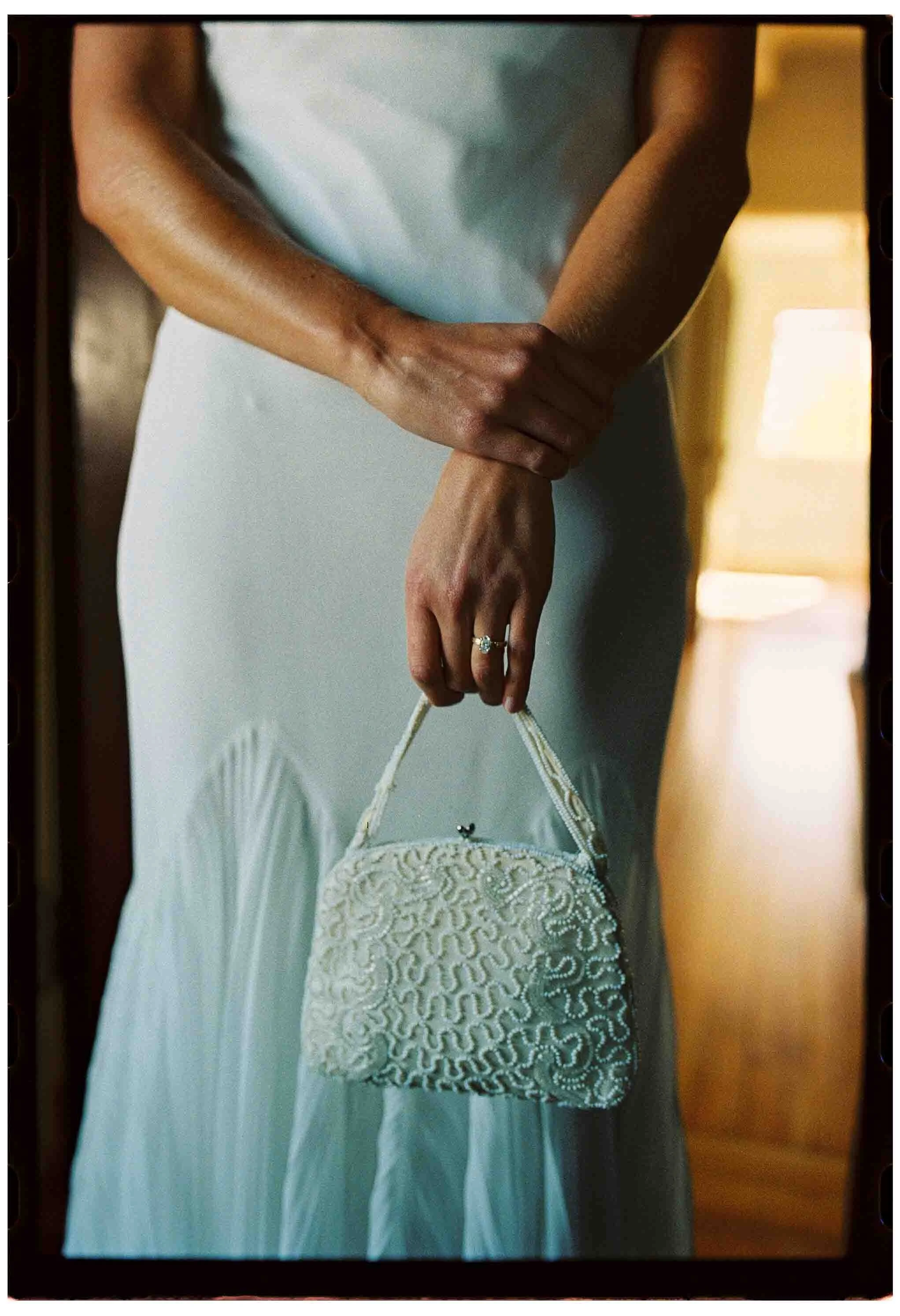 close up of bride's heirloom beaded clutch and engagement ring in front of wedding dress