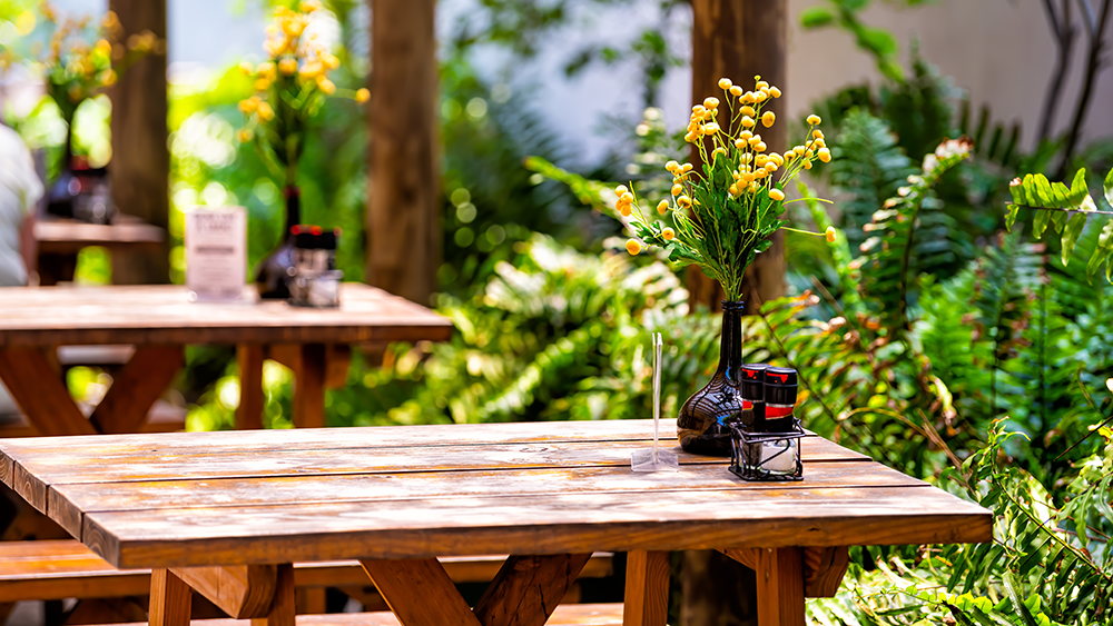 Outdoor restaurant patio tables with various plants. On the table is salt, pepper, and vinegar.