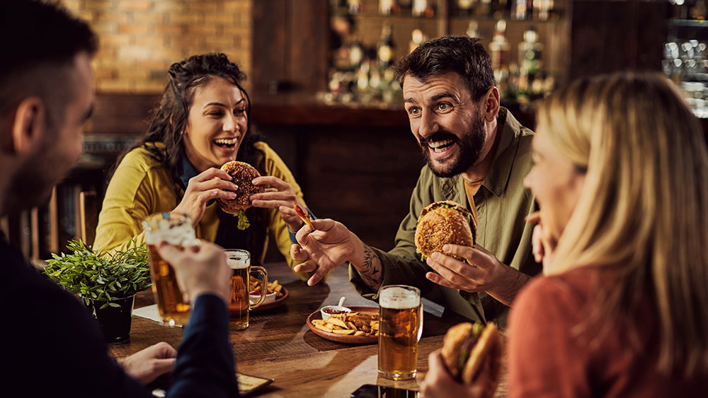 A group of friends eating burgers and beer at a small restaurant