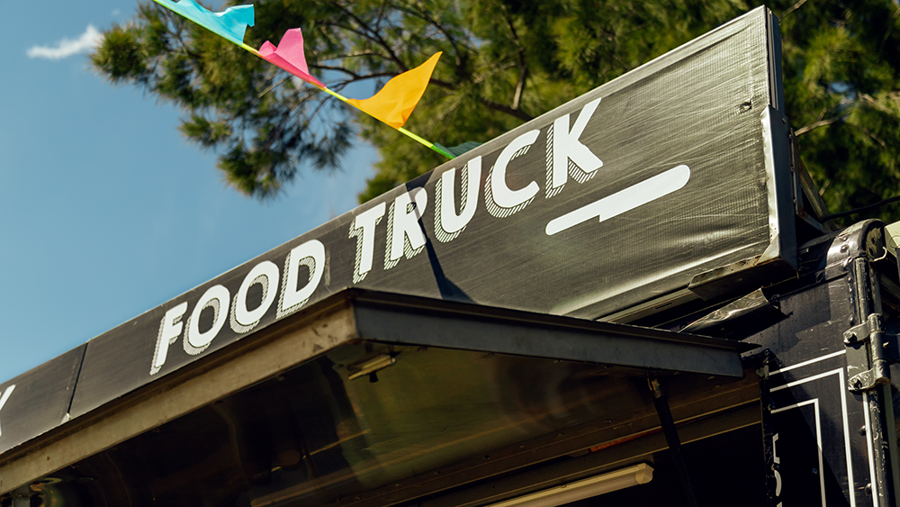 Close up of a food truck sign against a blue sky.
