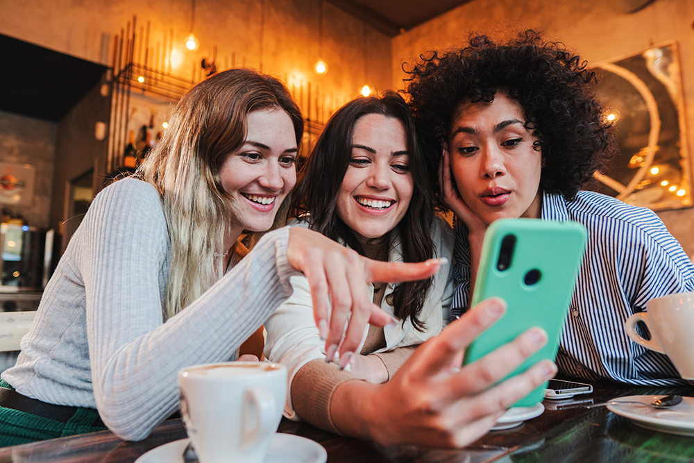 Three young women oogle at a smartphone in a restaurant