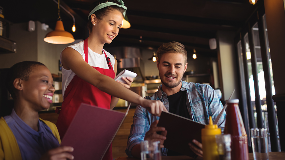 A waitress points out interesting restaurant menu items to two guests.