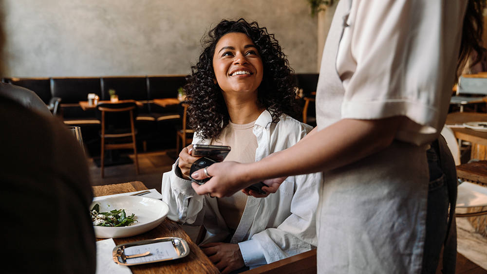 Smiling restaurant guest paying for her bill using their smartphone