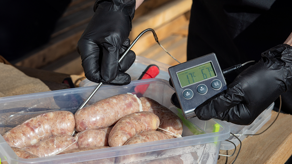 A food truck cook takes the food temperature of sausages.
