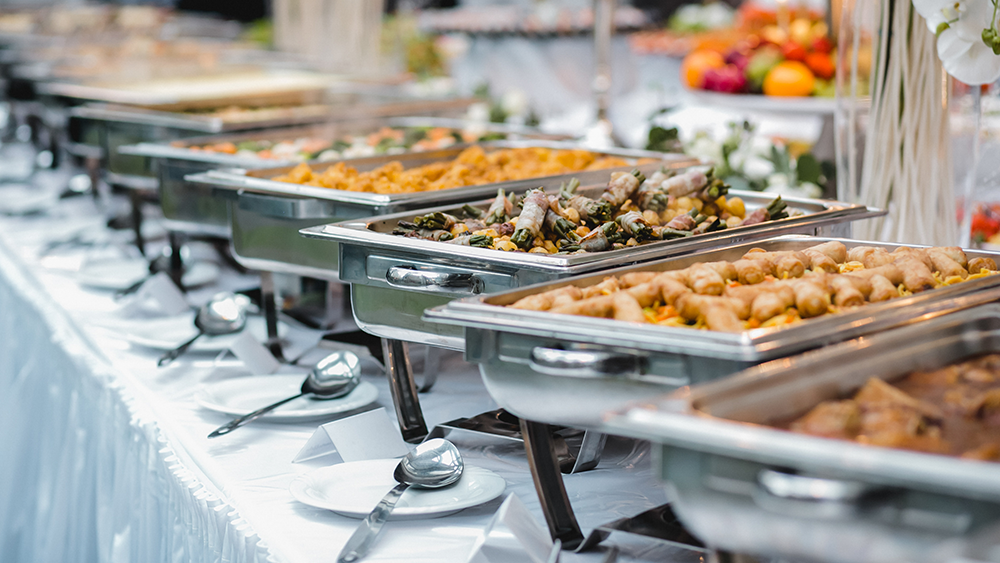 A bunch of catering pants in a row with various food items