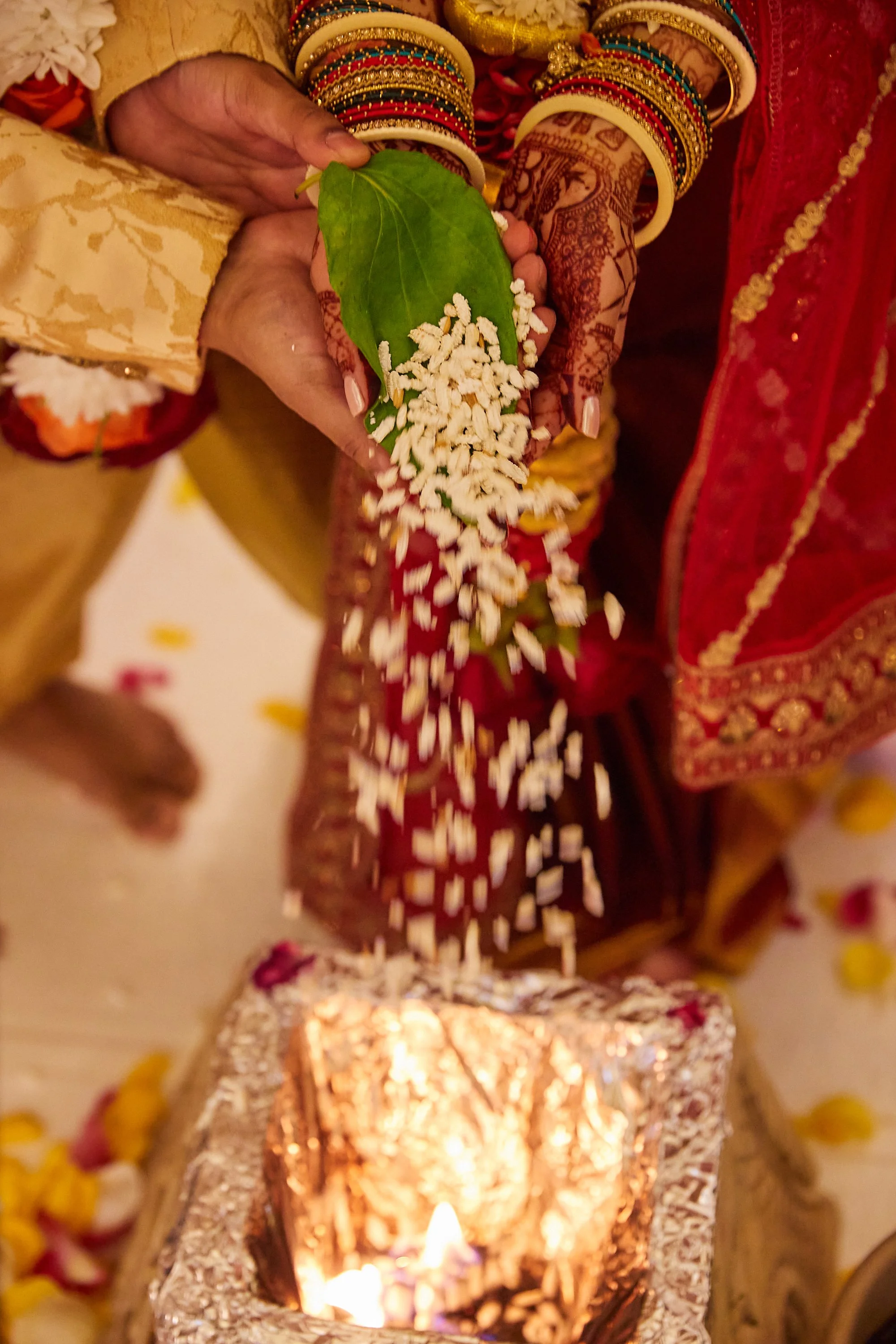 A person dressed in traditional Indian attire holding a green leaf with rice pouring onto it during a cultural ceremony.