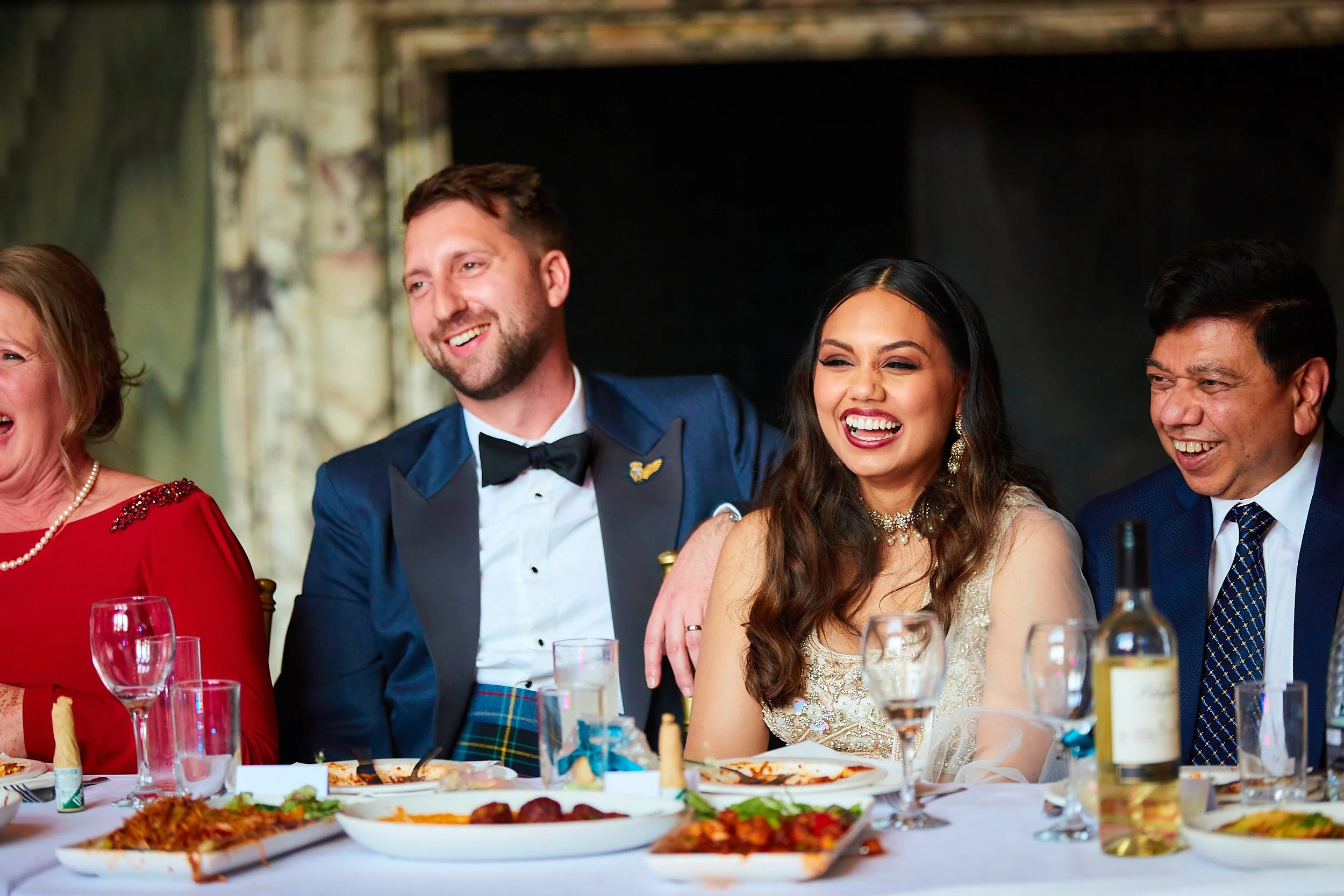 People sitting at a dinner table during a celebration, smiling and laughing, with food and drinks in front of them.
