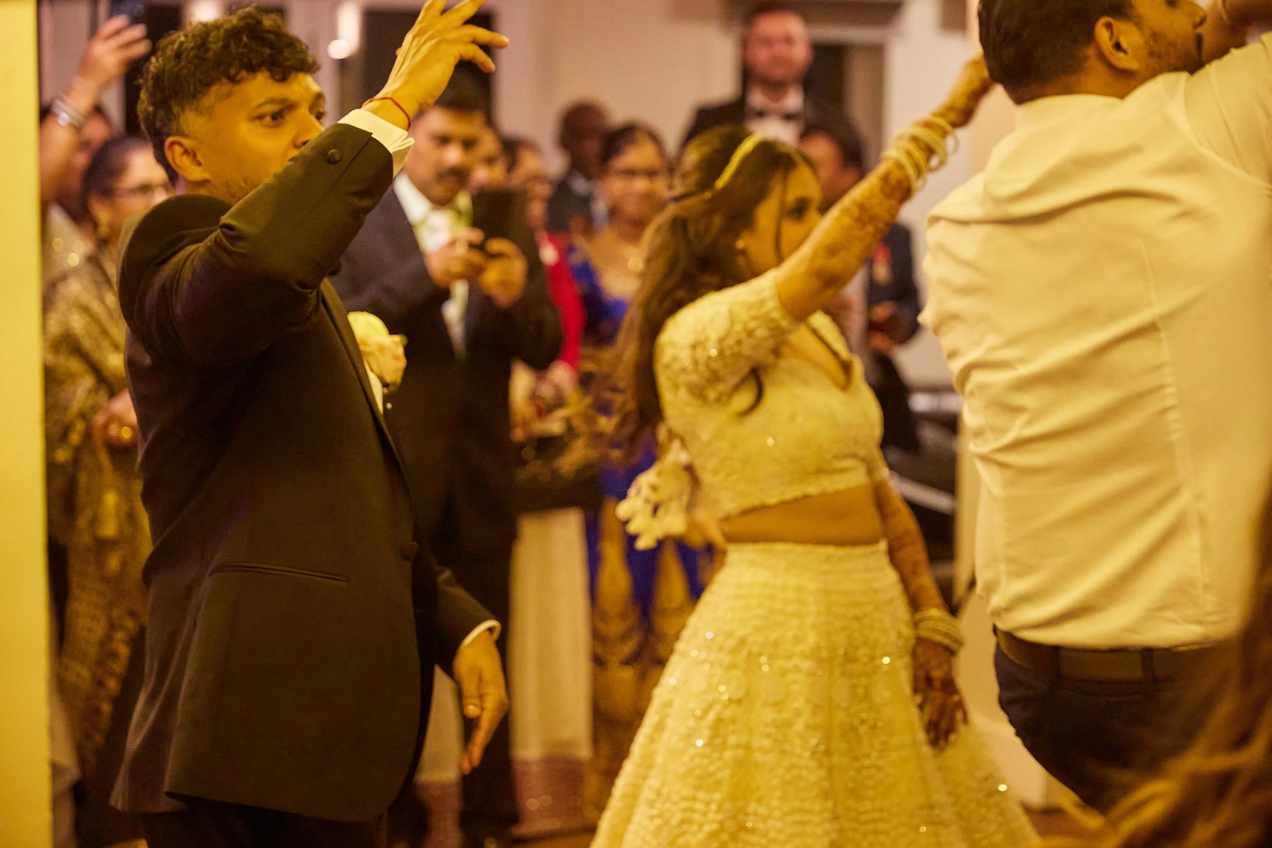 People dancing at a wedding celebration, with a groom and bride in traditional Indian attire