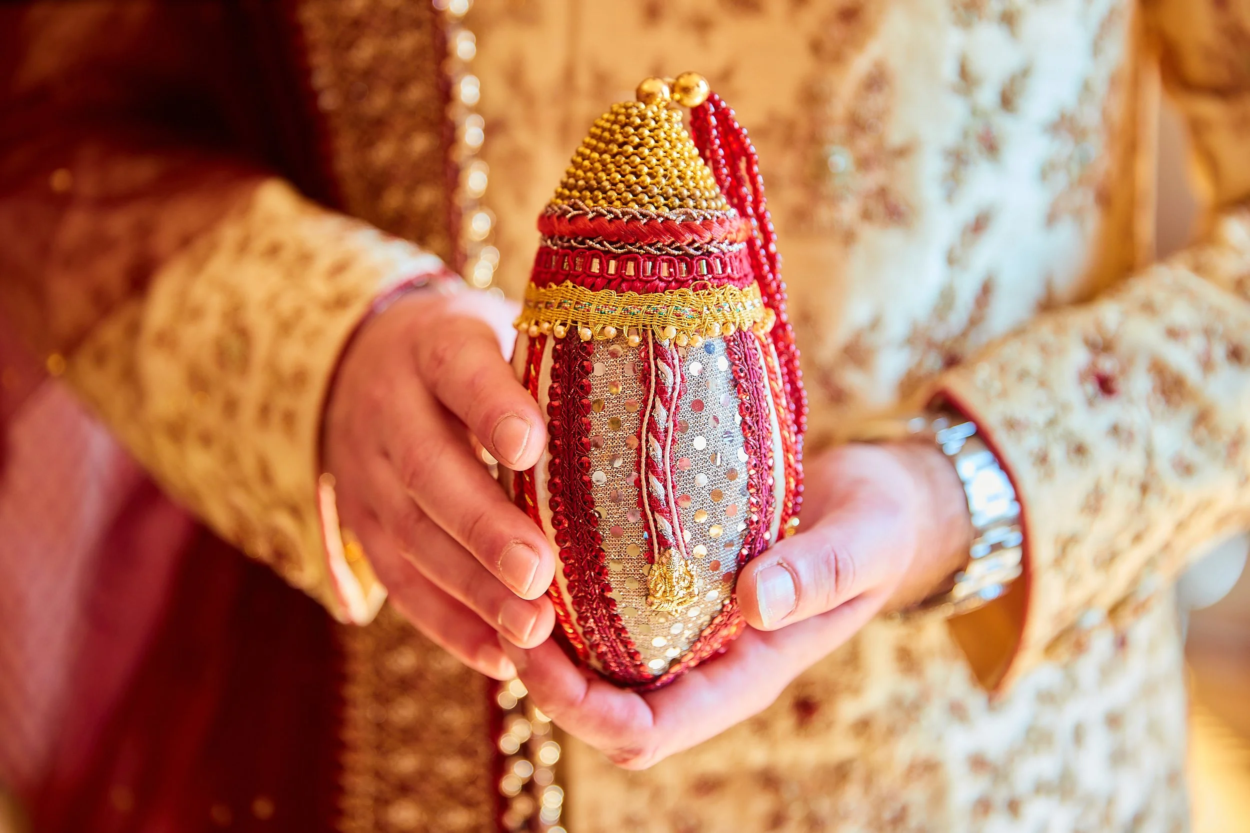 A person dressed in traditional Indian attire holding a decorative, bejeweled ornament.