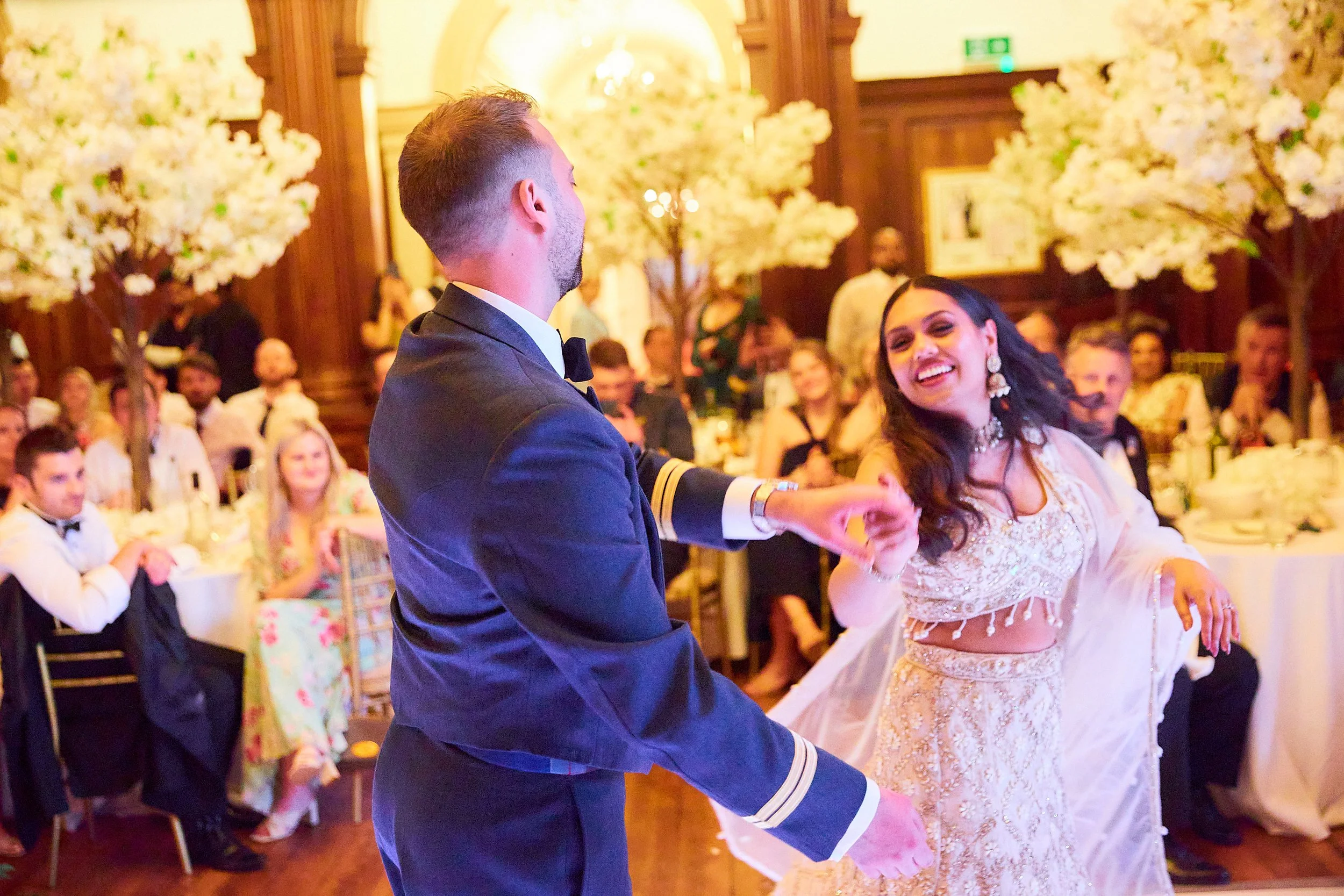 A bride and groom dancing at their wedding reception, with guests seated at tables in the background.