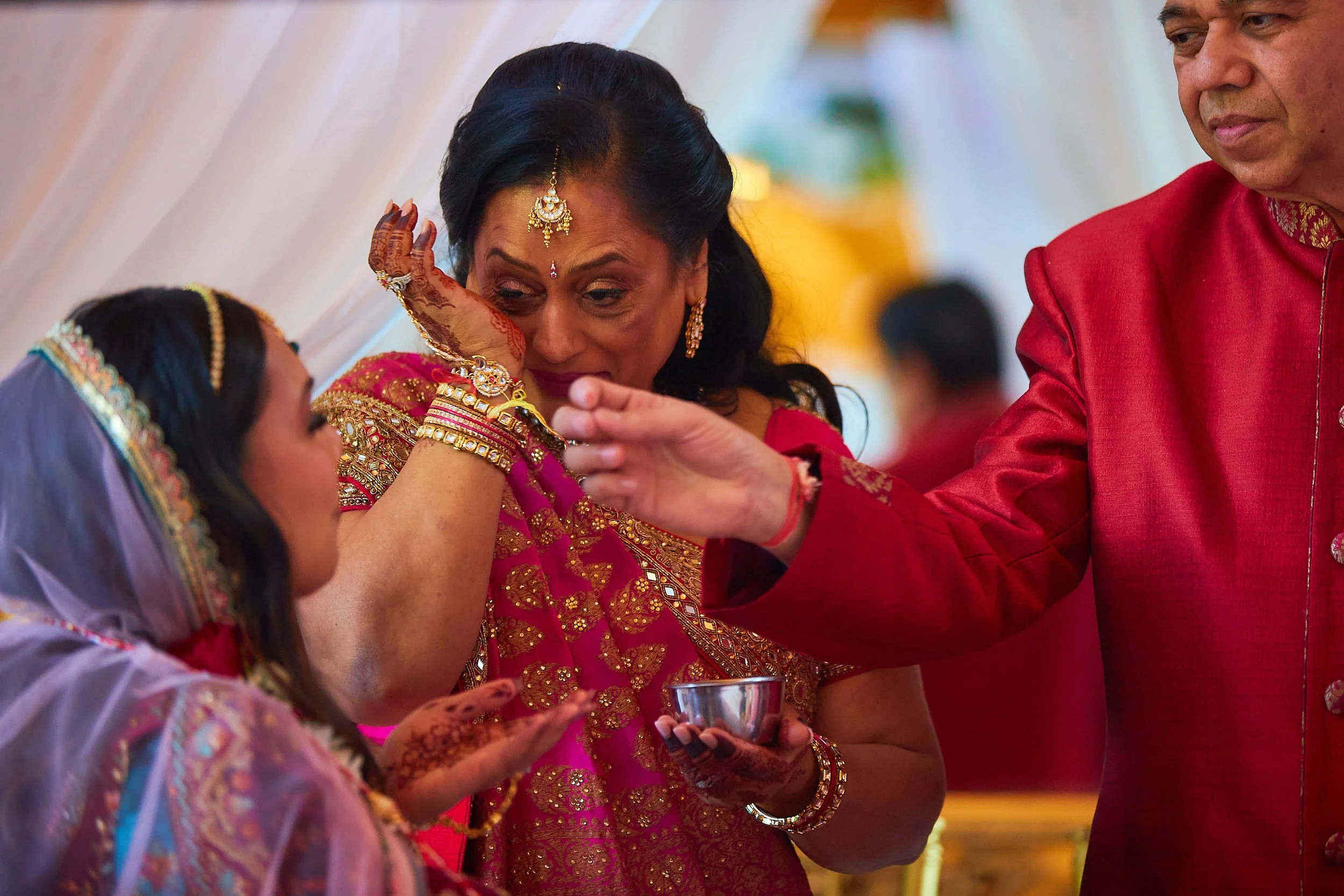 Indian wedding ceremony with family members in traditional attire, including a woman crying as she wipes her tears with her hand.