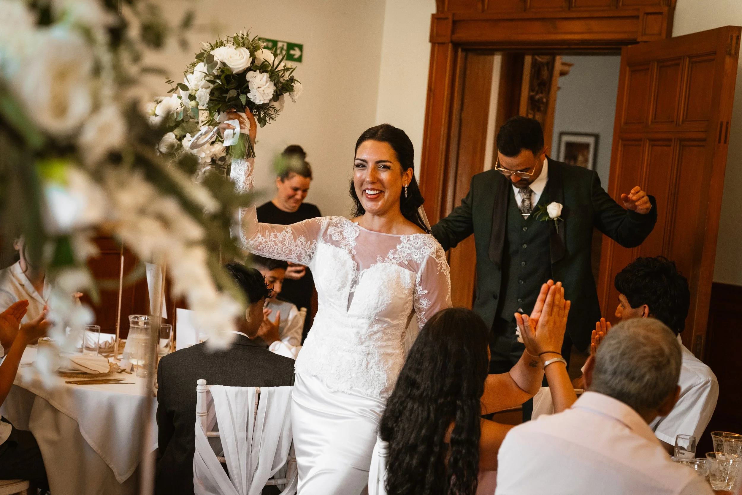 Bride and groom dancing at their wedding reception, surrounded by guests seated at tables with white tablecloths and floral centerpieces.