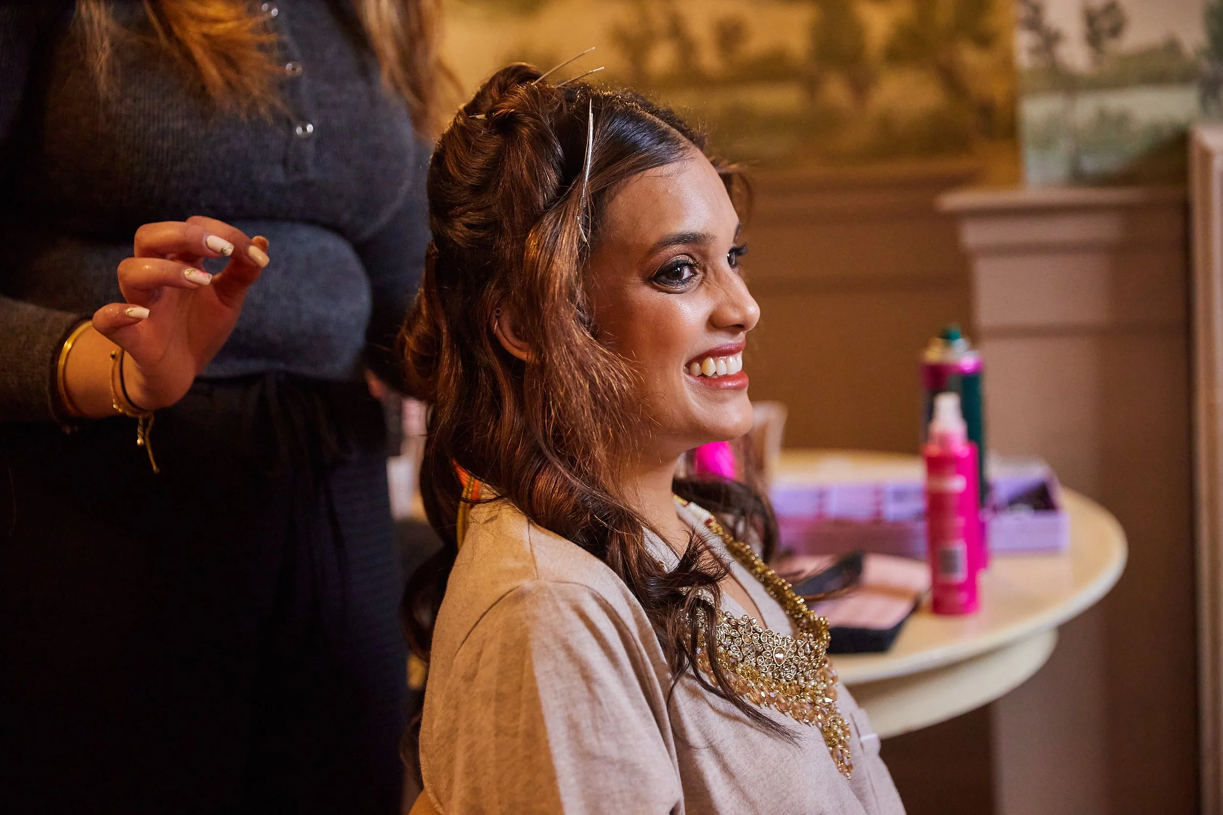 A woman with long, wavy curly hair smiling as she gets her hair styled at a salon.