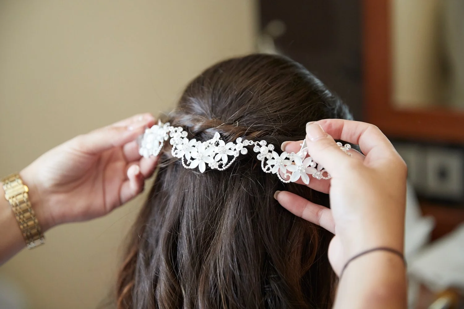 Person placing a floral tiara on a woman's brown hair.