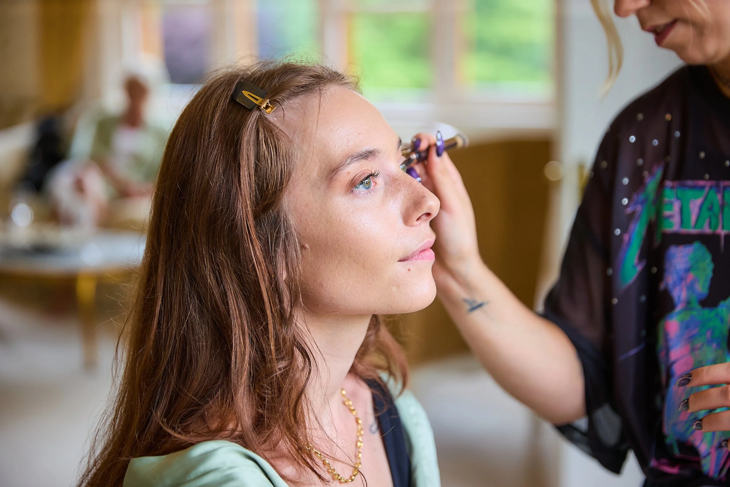 A woman with long red hair getting her makeup done by a makeup artist.