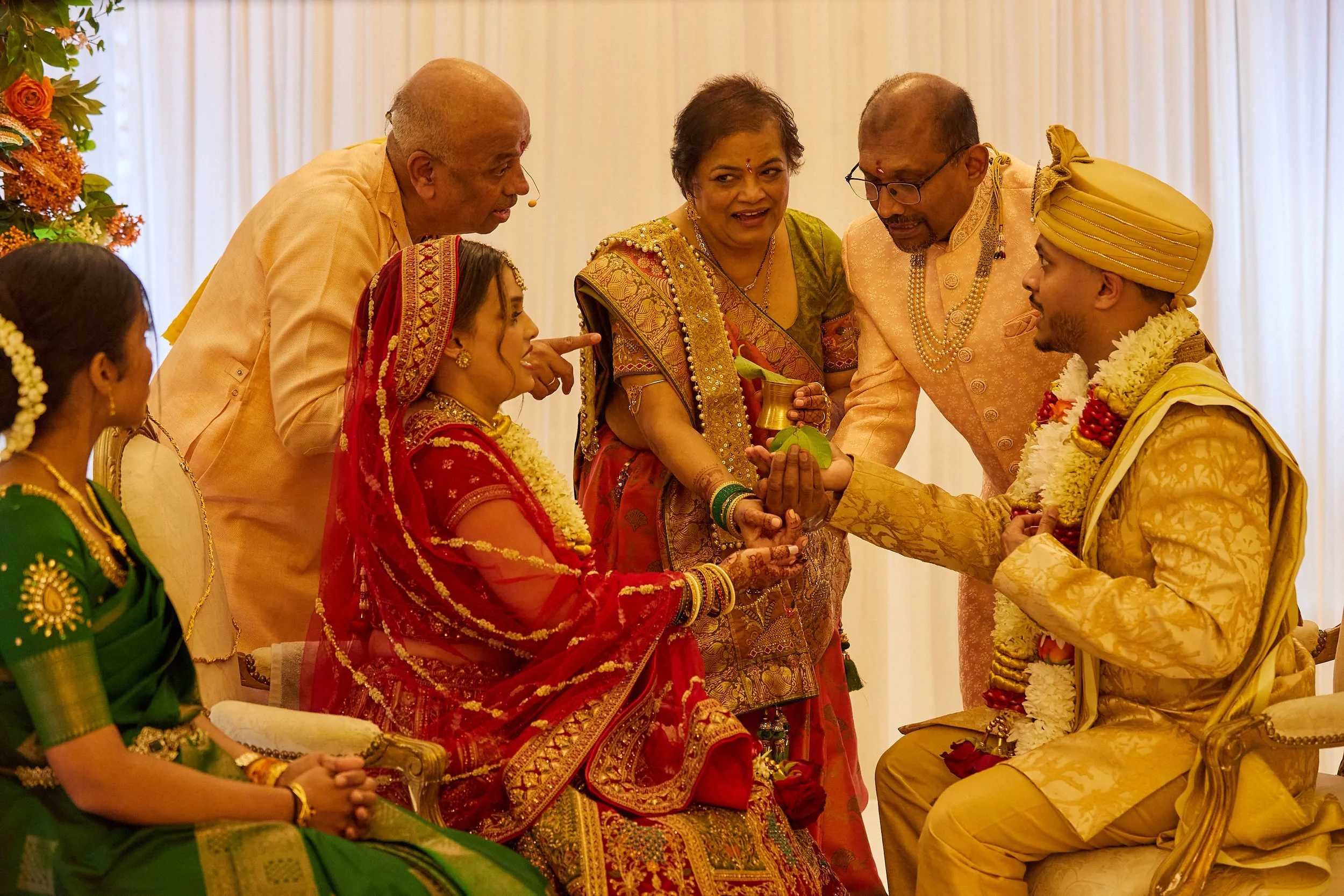Indian wedding ceremony with family members, bride and groom exchanging garlands, dressed in traditional attire, surrounded by relatives.