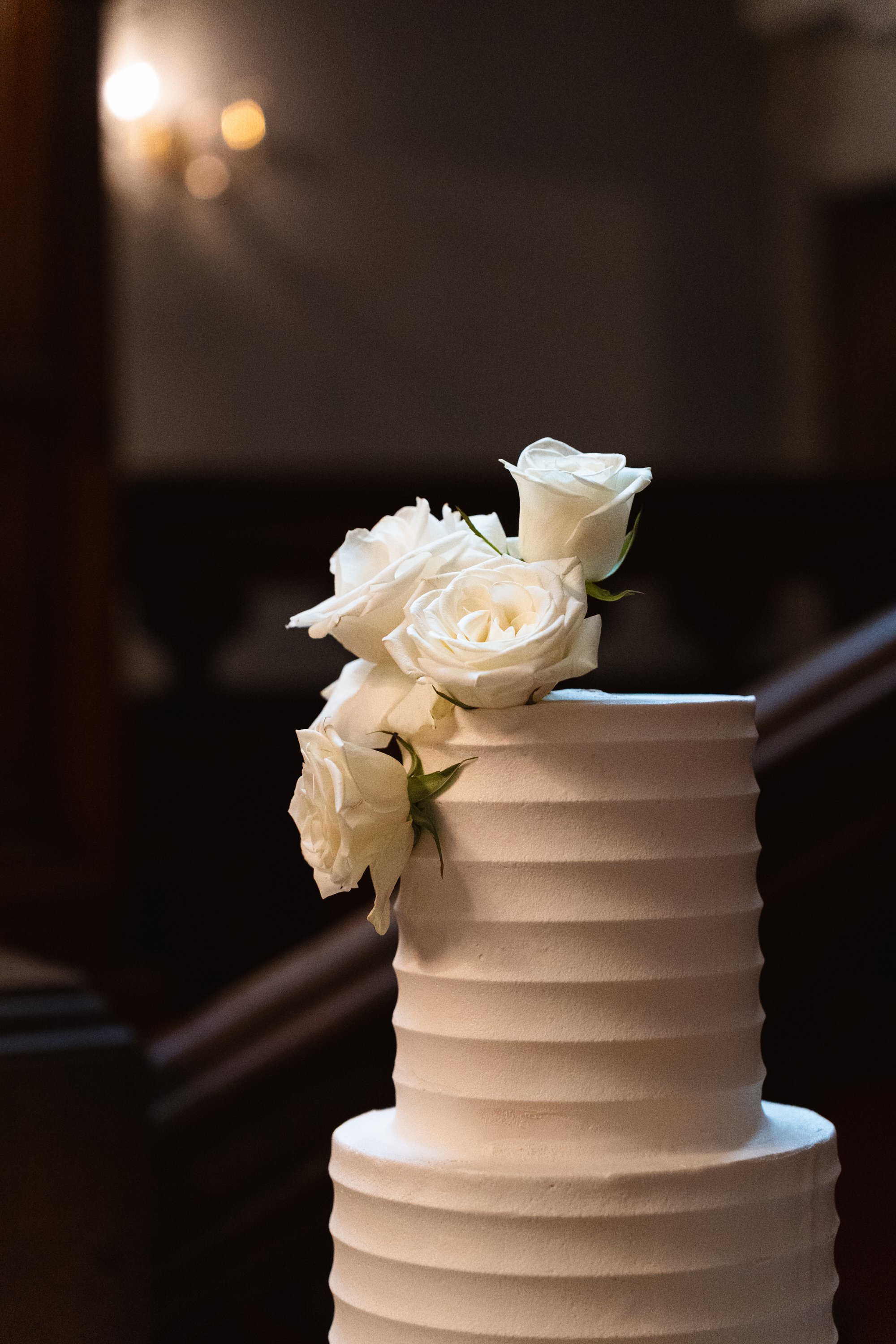 A white wedding cake with a textured, wavy surface and white roses on top