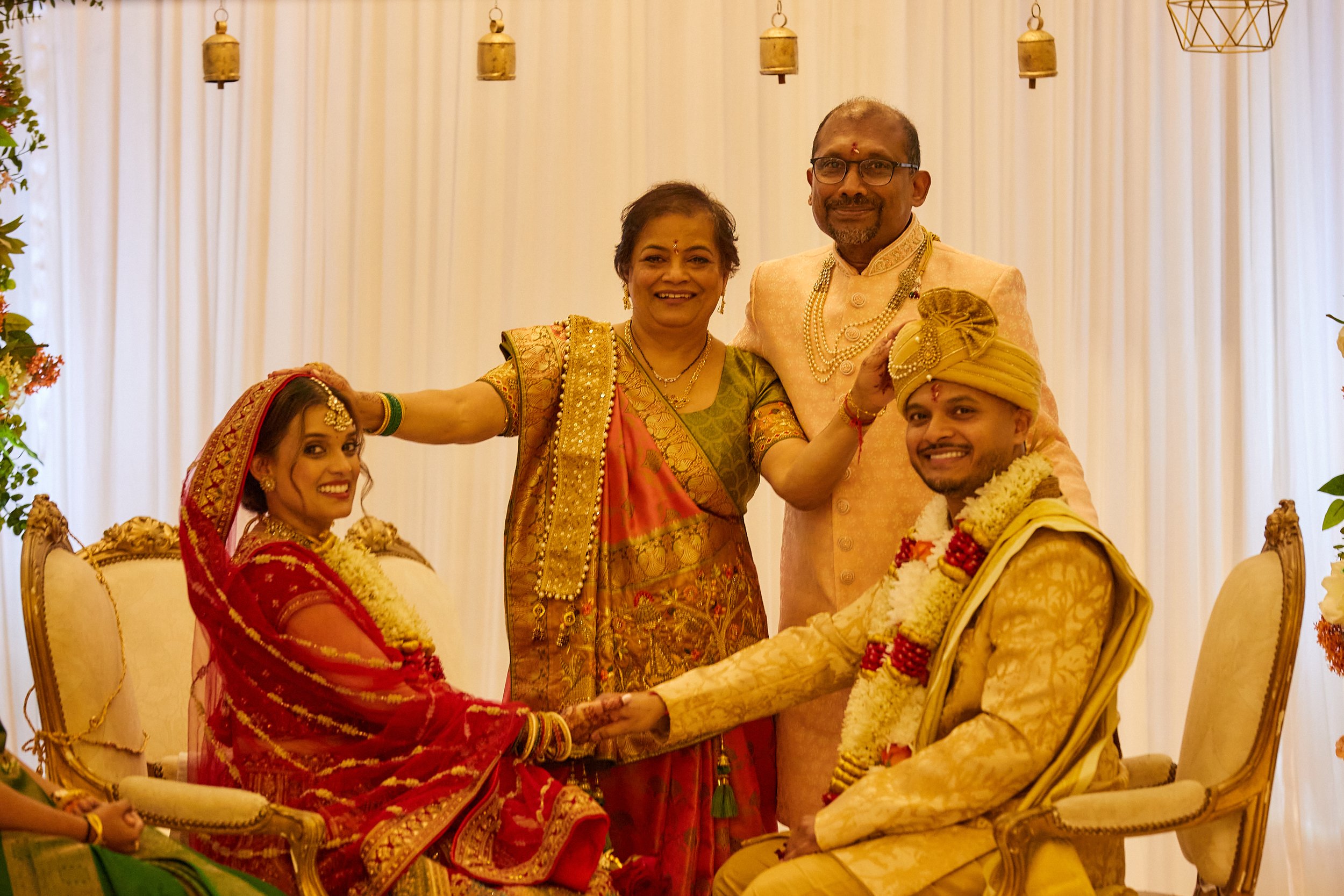 A traditional Indian wedding ceremony with bride, groom, and family members dressed in colorful attire, smiling in front of a decorated backdrop.