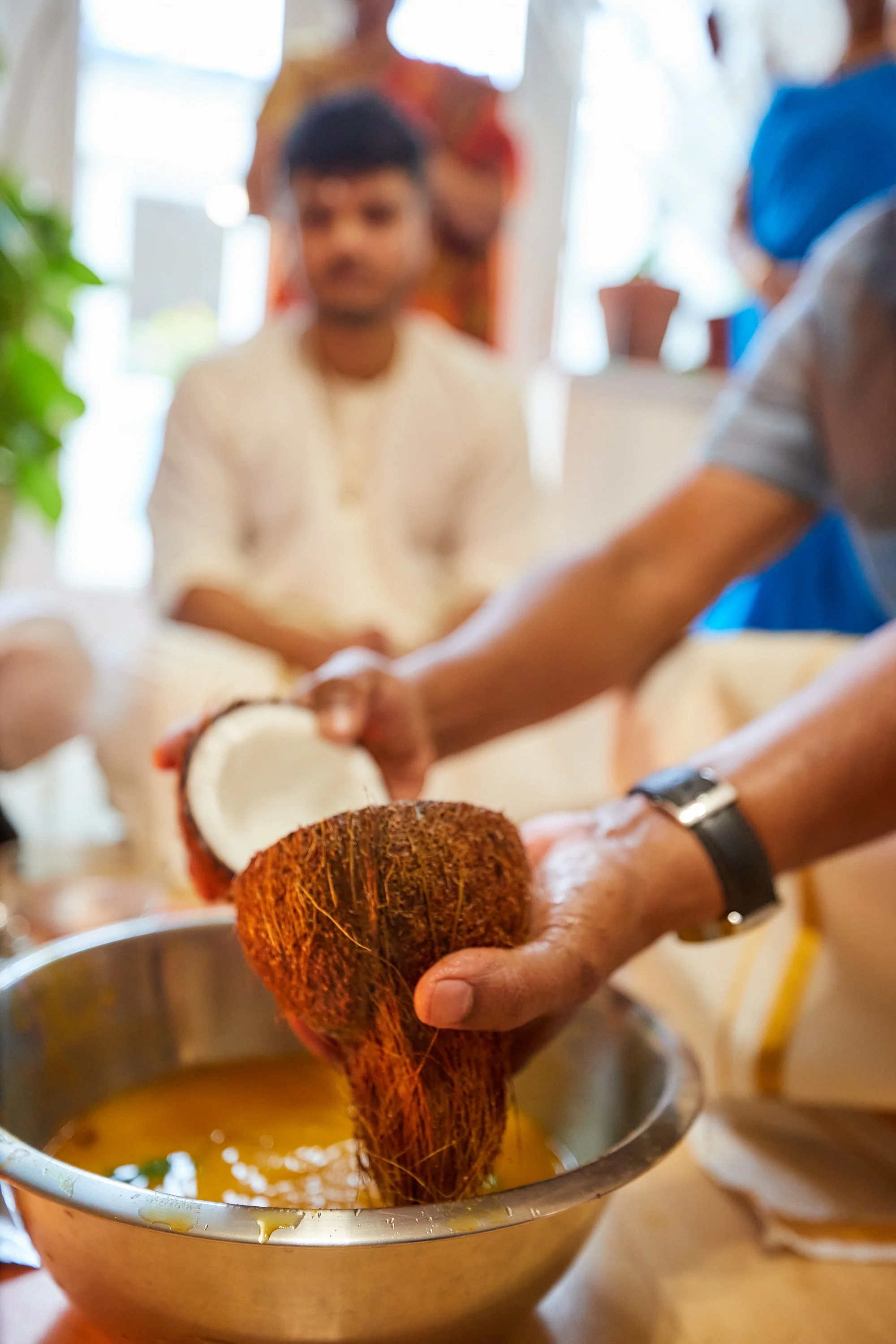 Person squeezing coconut into a bowl of liquid during a cooking or food preparation process.
