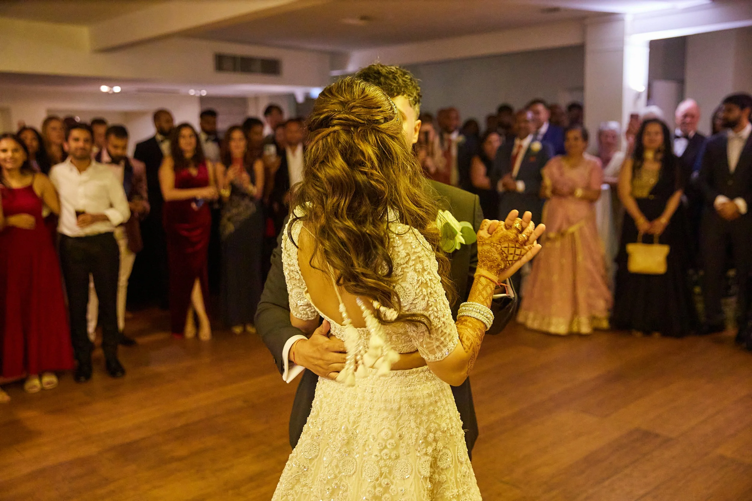 A bride and groom dancing at their wedding with a crowd of guests watching in the background.