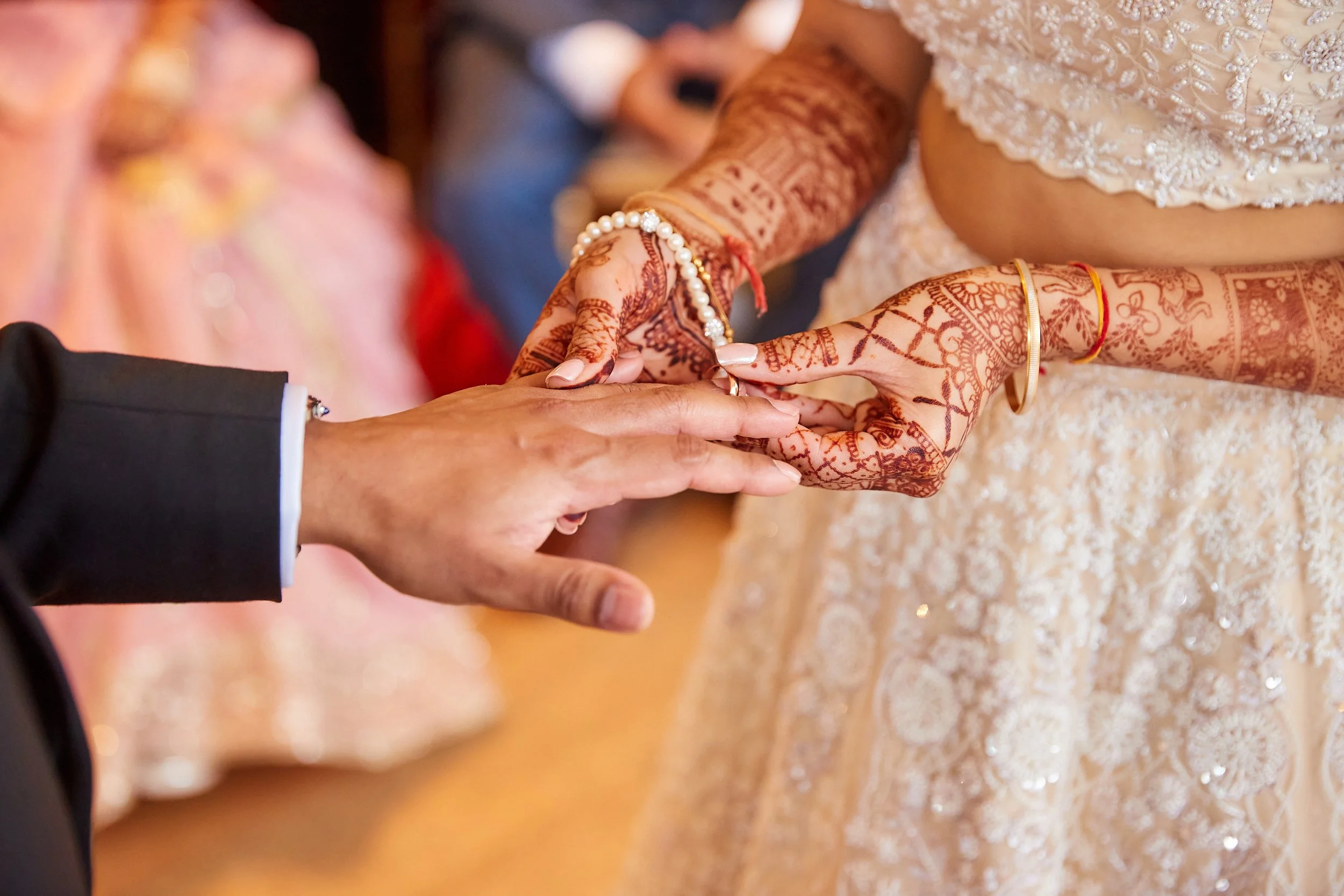 Bride and groom holding hands during a wedding ceremony, with the bride wearing intricate henna, jewelry, and a lace dress.