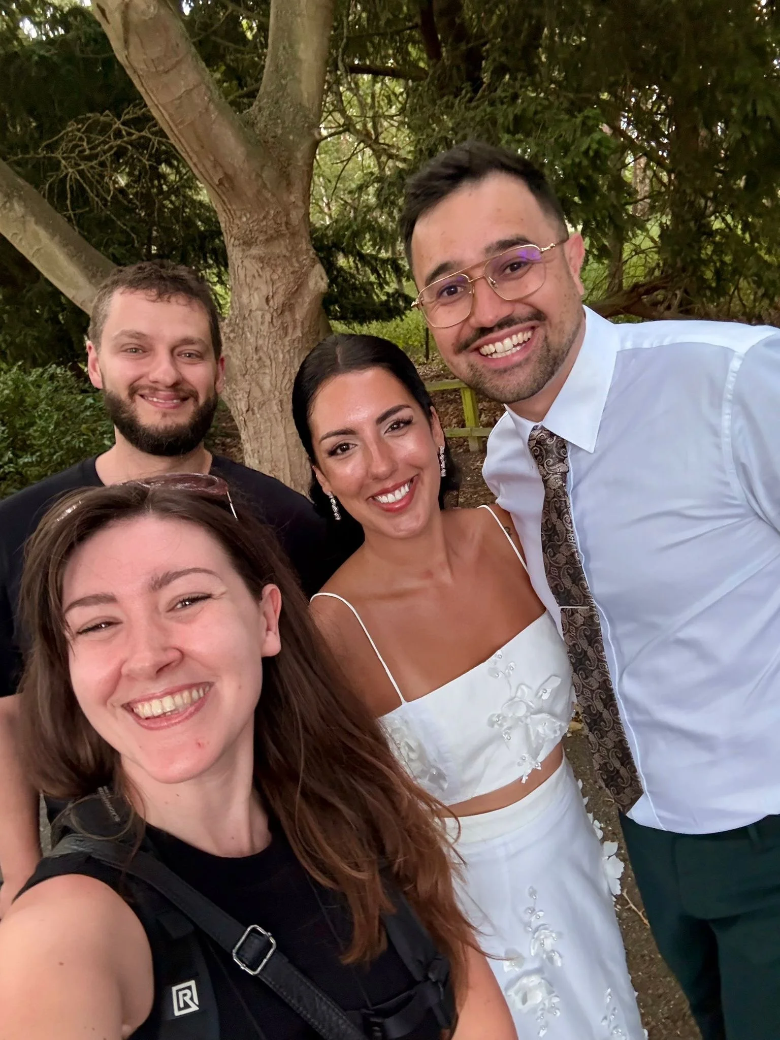 Group of four friends taking a selfie outdoors near a large tree.