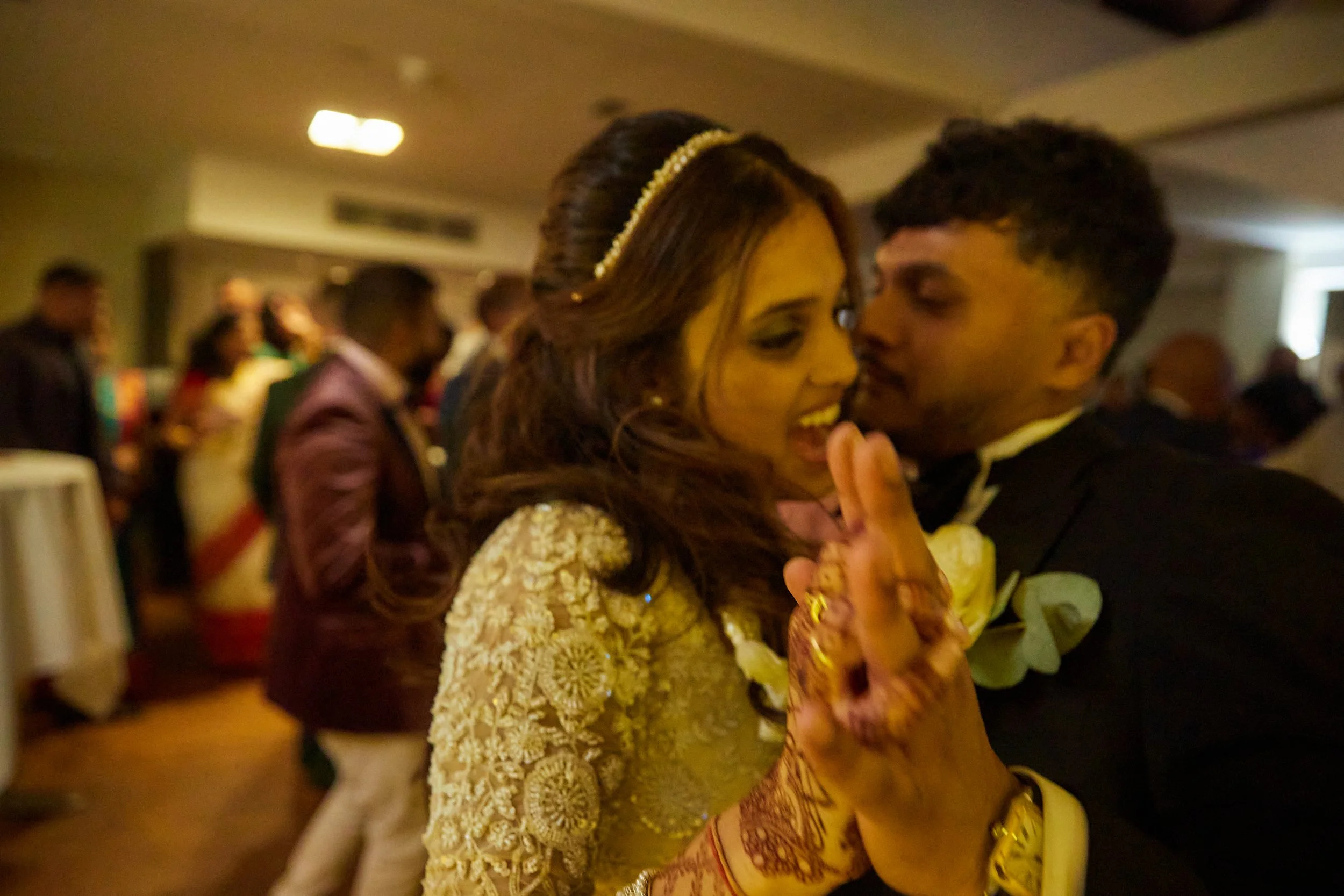 A couple dancing closely at a wedding reception, surrounded by guests in the background.