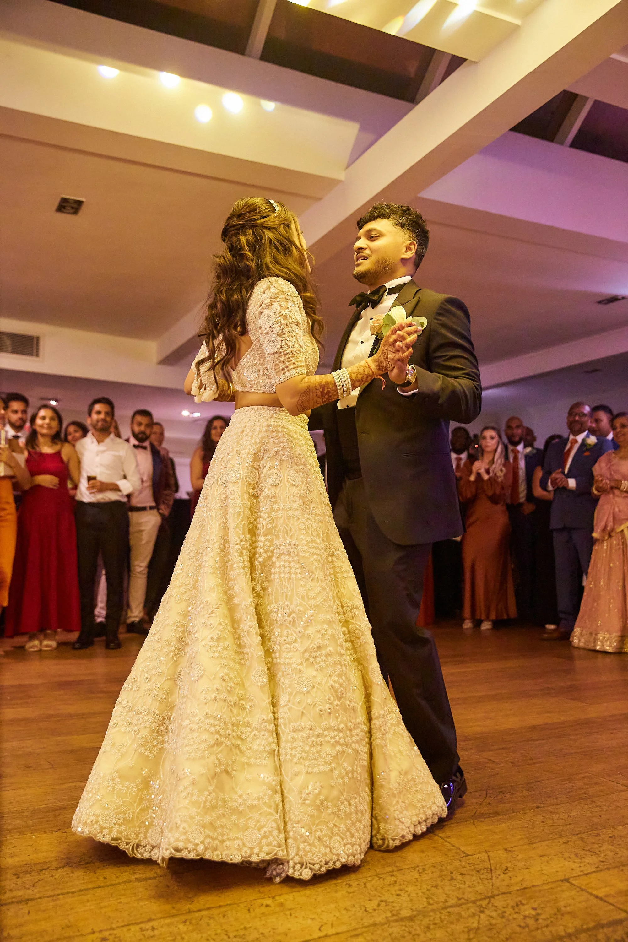 A bride and groom dance together at their wedding reception, surrounded by guests.