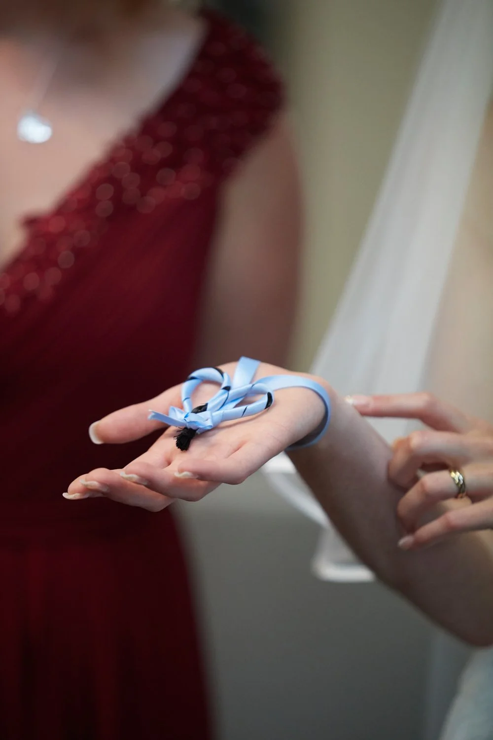 A person wearing a ring holds a gift with a blue ribbon bow.