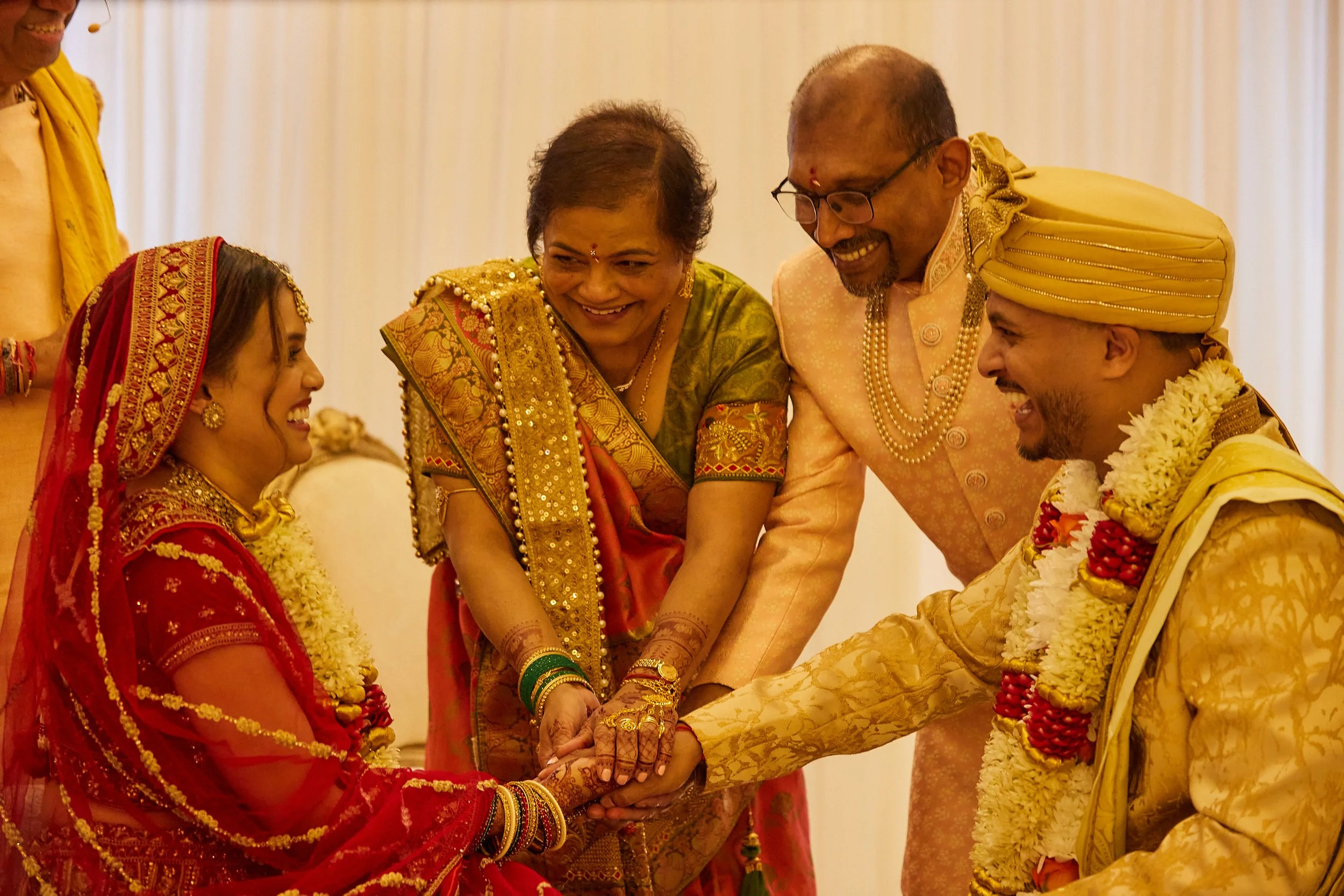 Indian wedding ceremony with bride and groom exchanging rings, surrounded by family members in traditional attire.