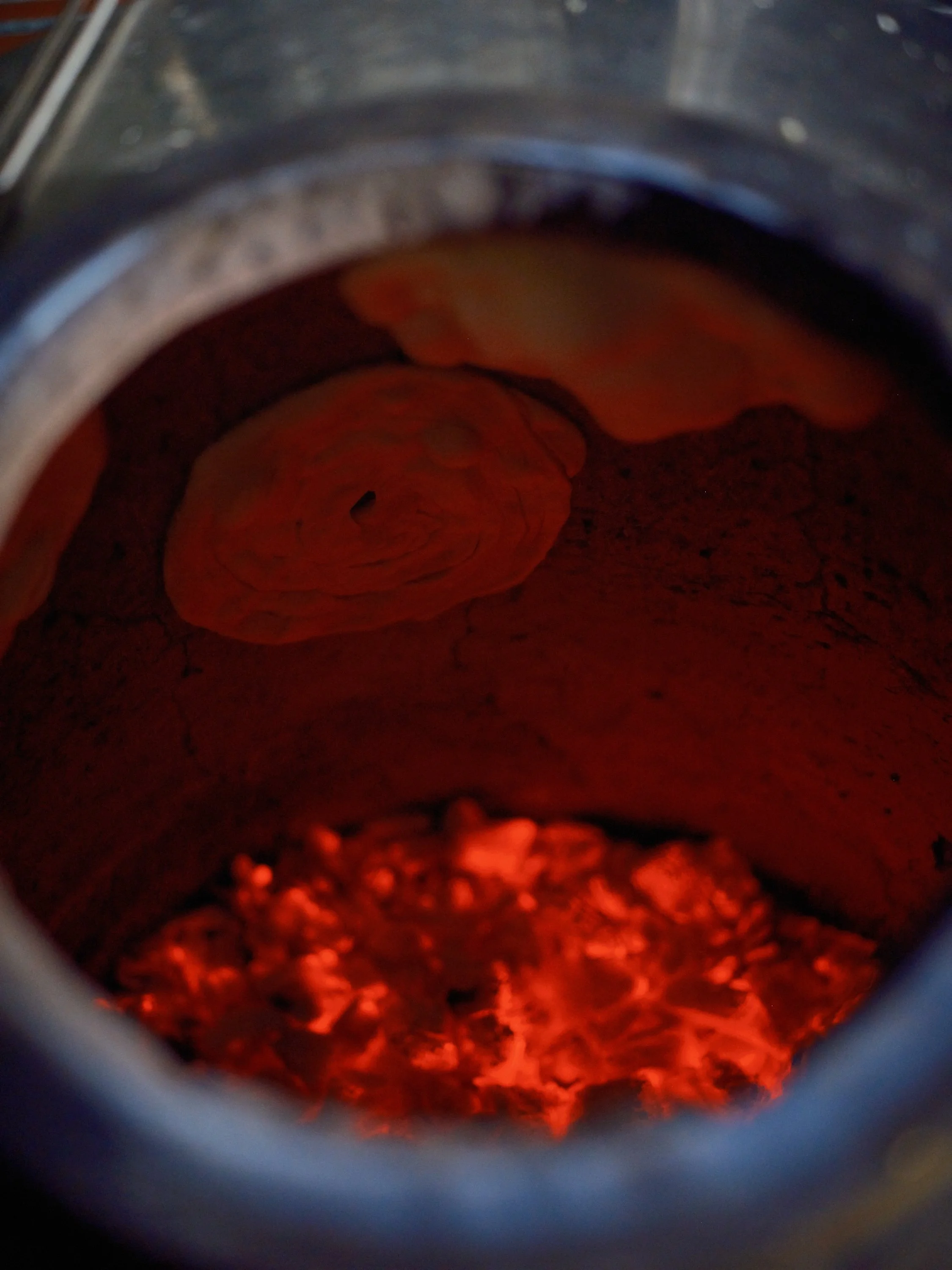 The inside of a charcoal grill with glowing hot coals and some partially burnt wood pieces.
