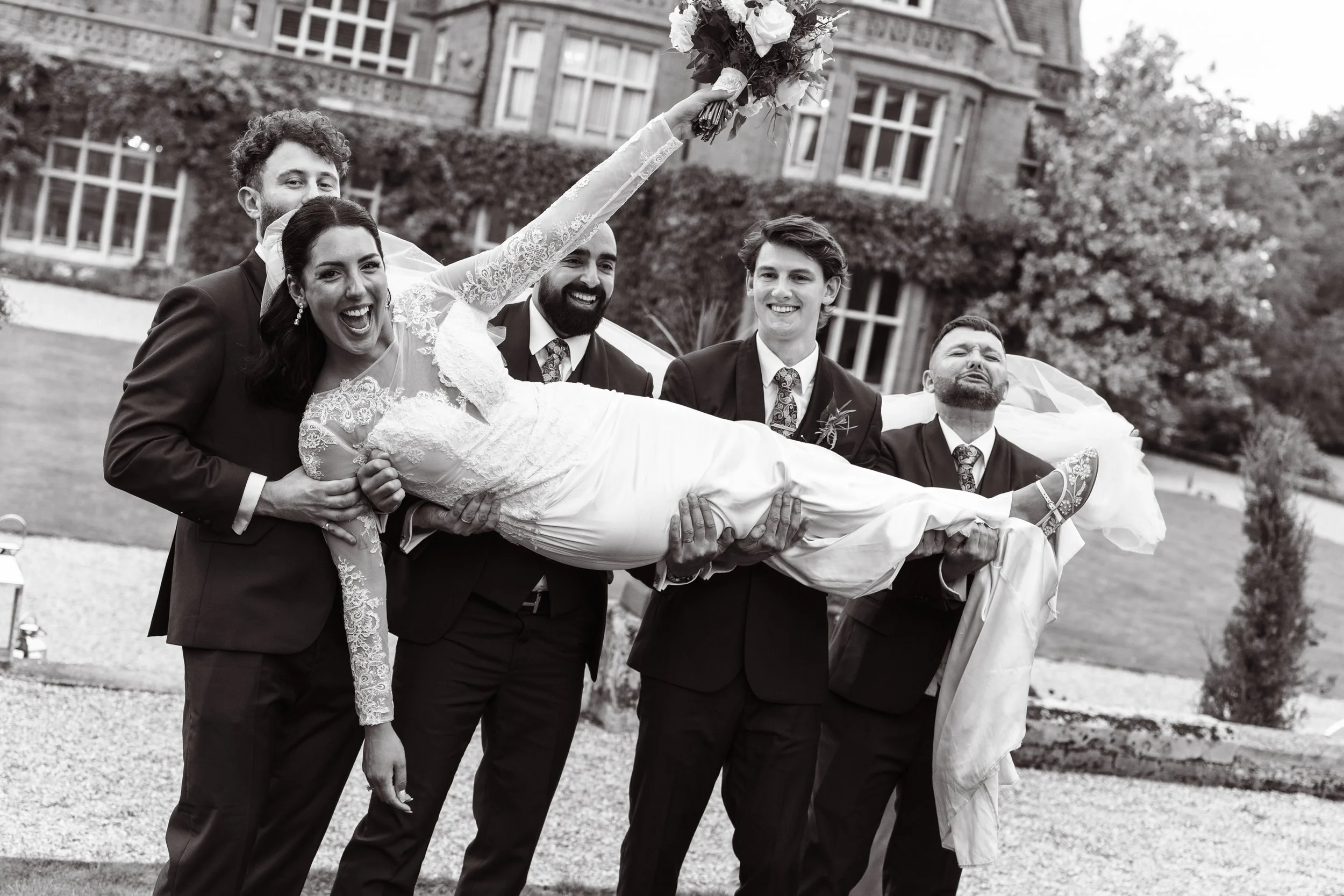 A woman in a wedding dress being carried by five men in suits during a wedding celebration.