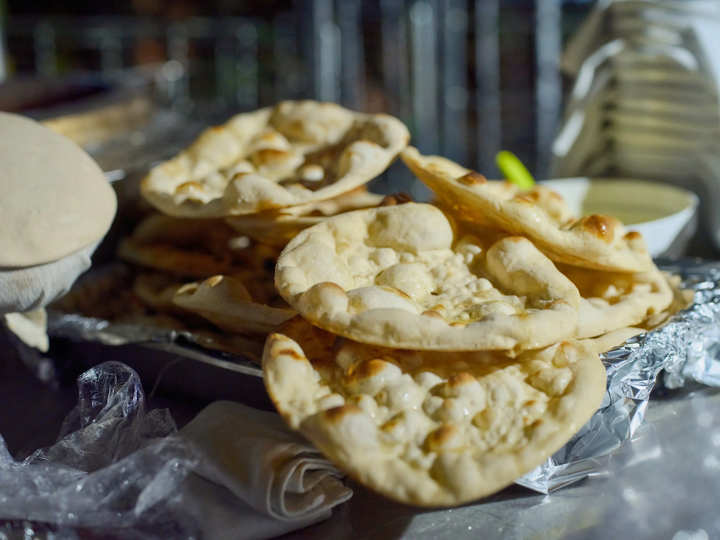 Close-up of freshly baked naan bread stacked on a foil-lined tray at a food stall or restaurant.