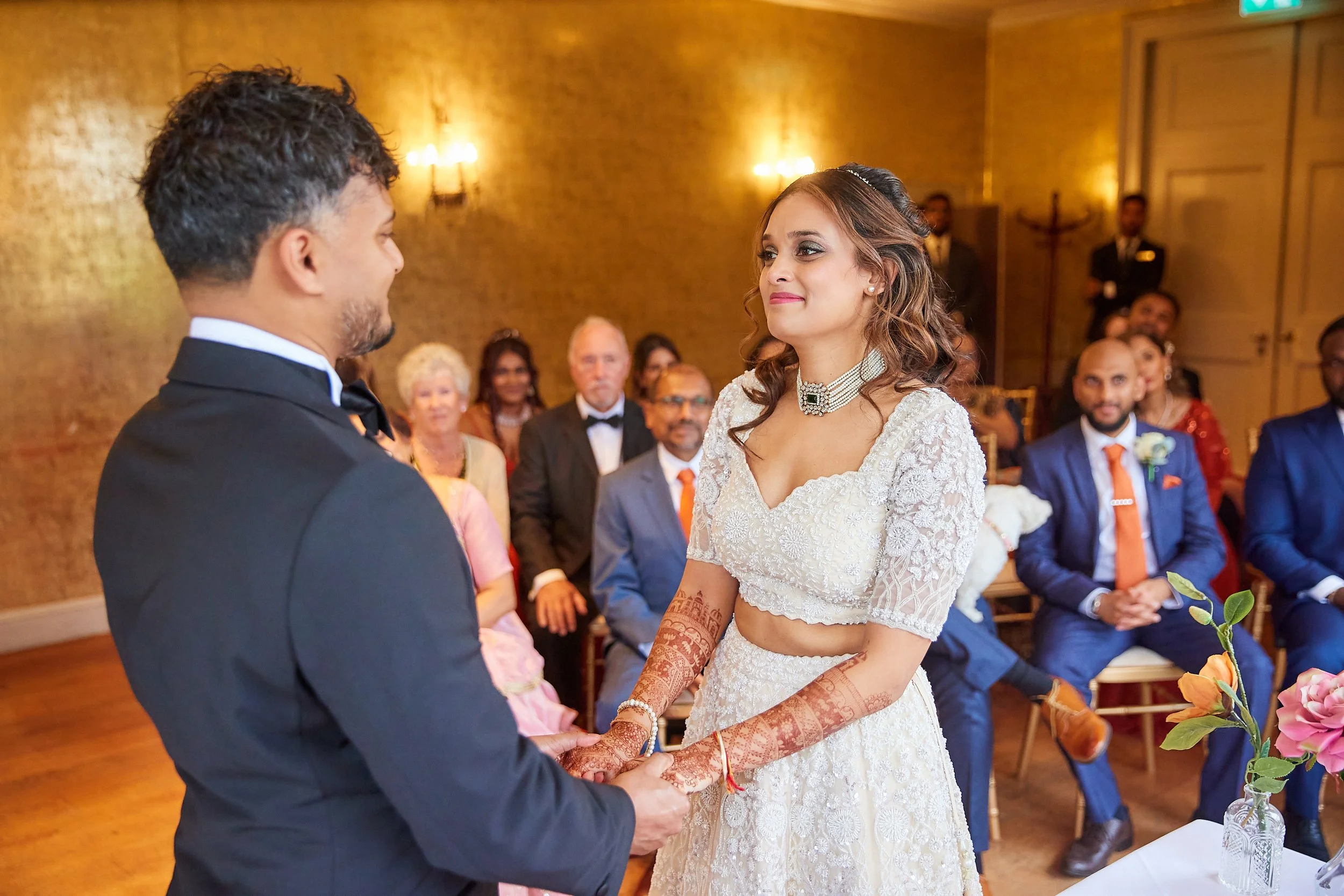 Bride and groom holding hands during wedding ceremony with guests in background.
