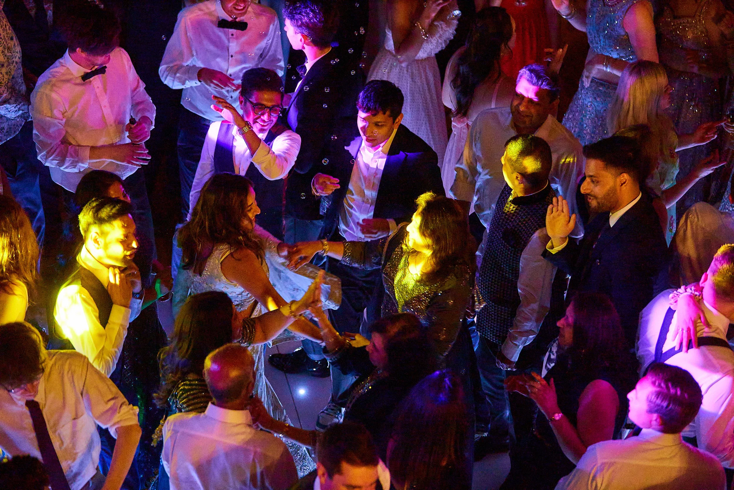 People dancing and enjoying at a lively party or celebration, with colorful lighting and formal attire.