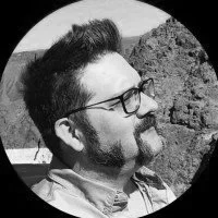 Side profile of a man with glasses and facial hair outdoors.