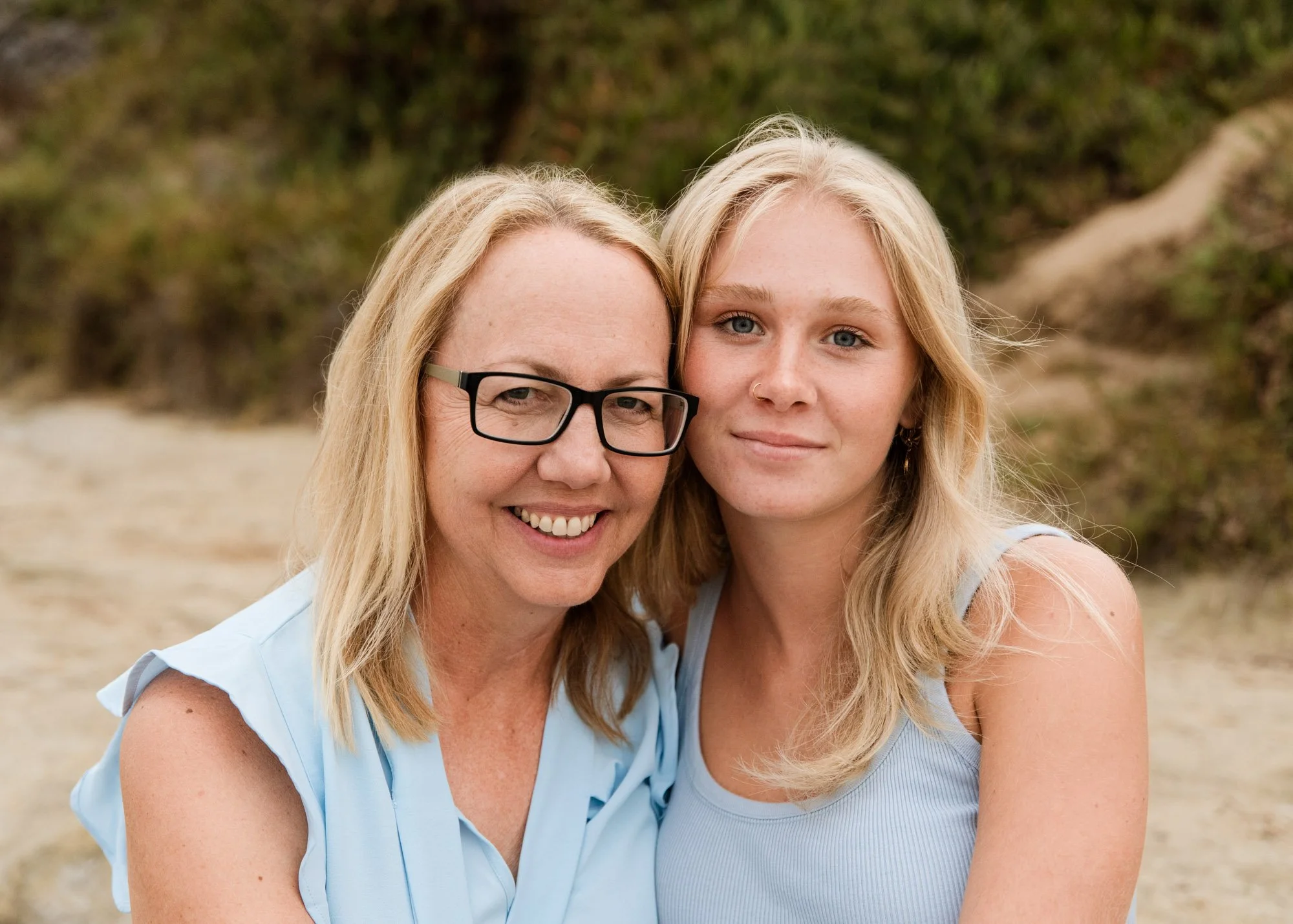 Close-up portrait of mom and teenage daughter, both with blond hair wearing light blue shirts in San Diego