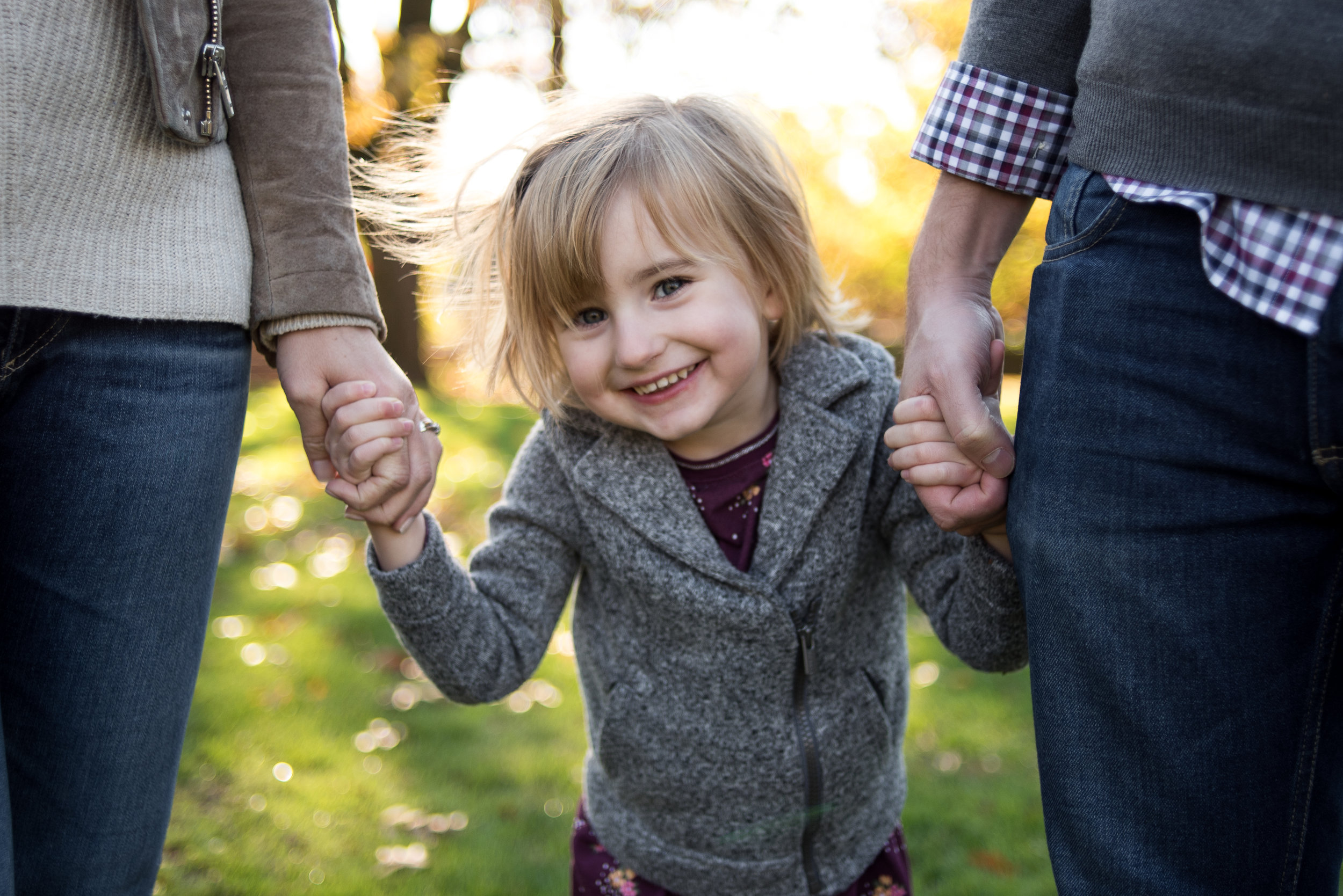 Close up of young girl holding parents hands in Portland park