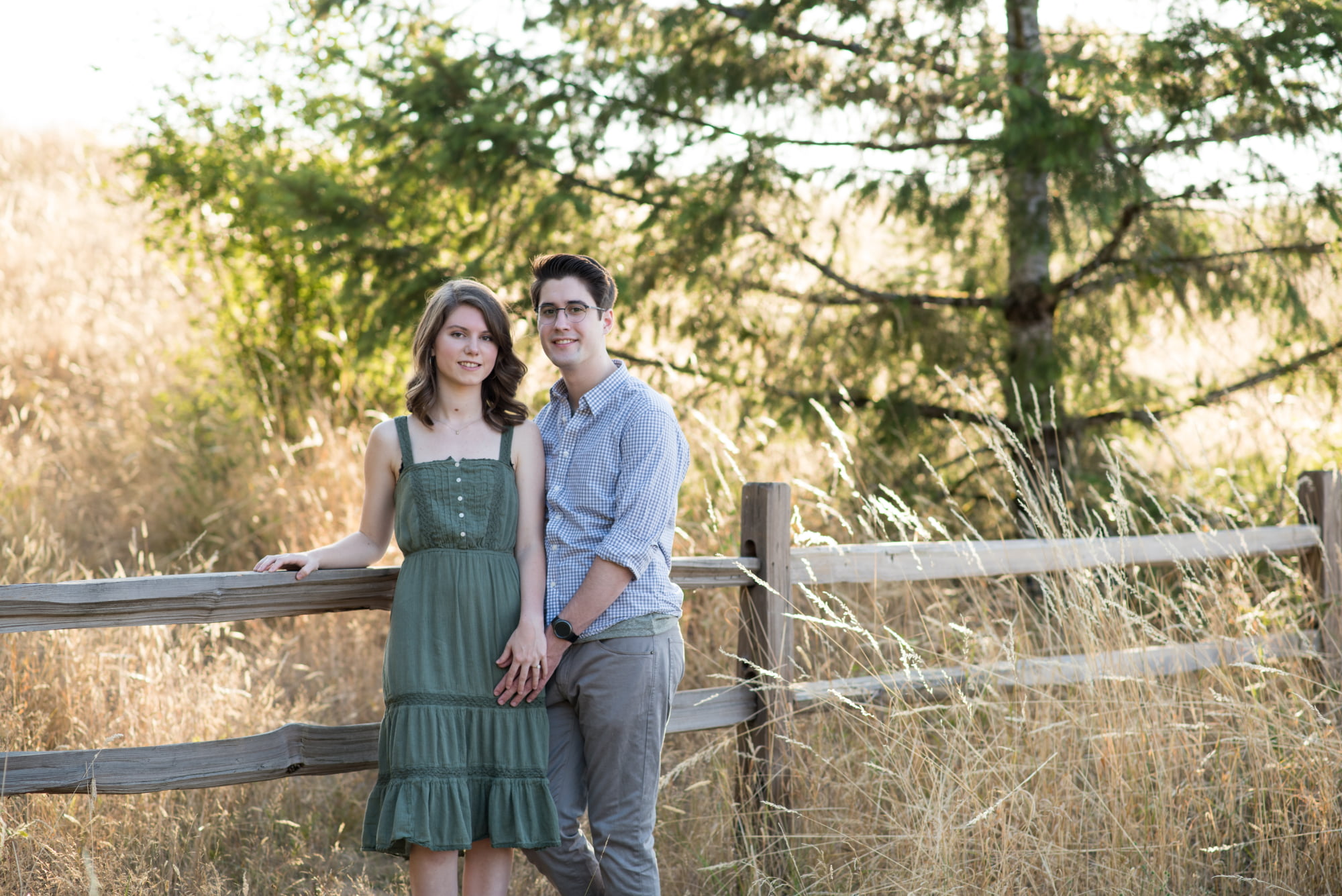 Engaged couple leaning on wooden fence