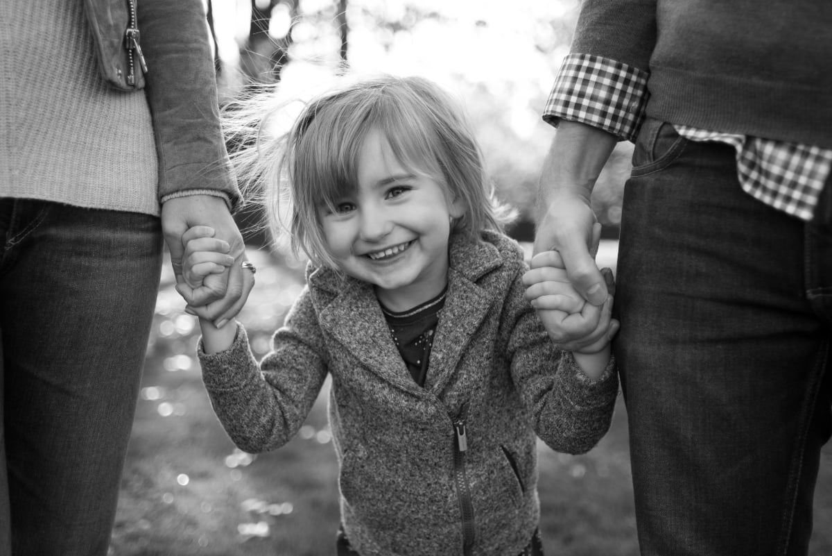 Black and white photo of girl holding parents hands in Portland