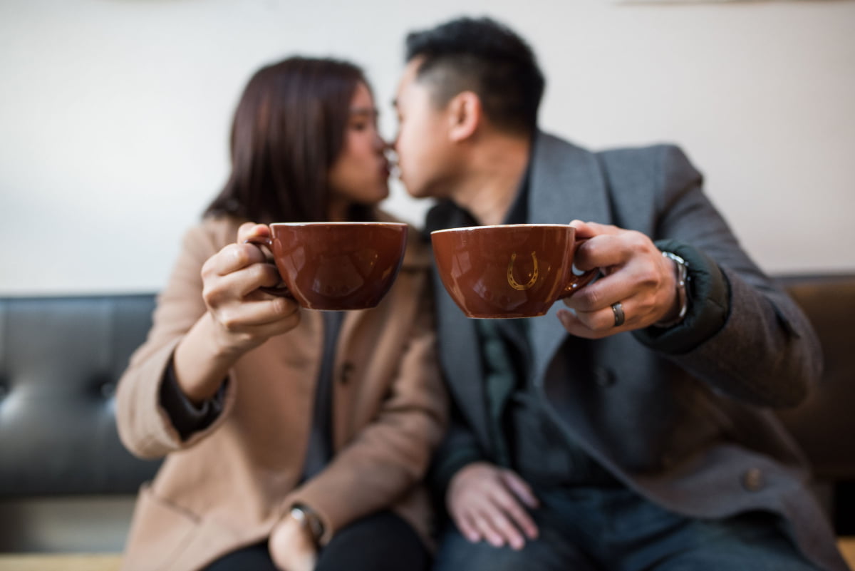 Couple kissing and holding coffee mugs at Stumptown