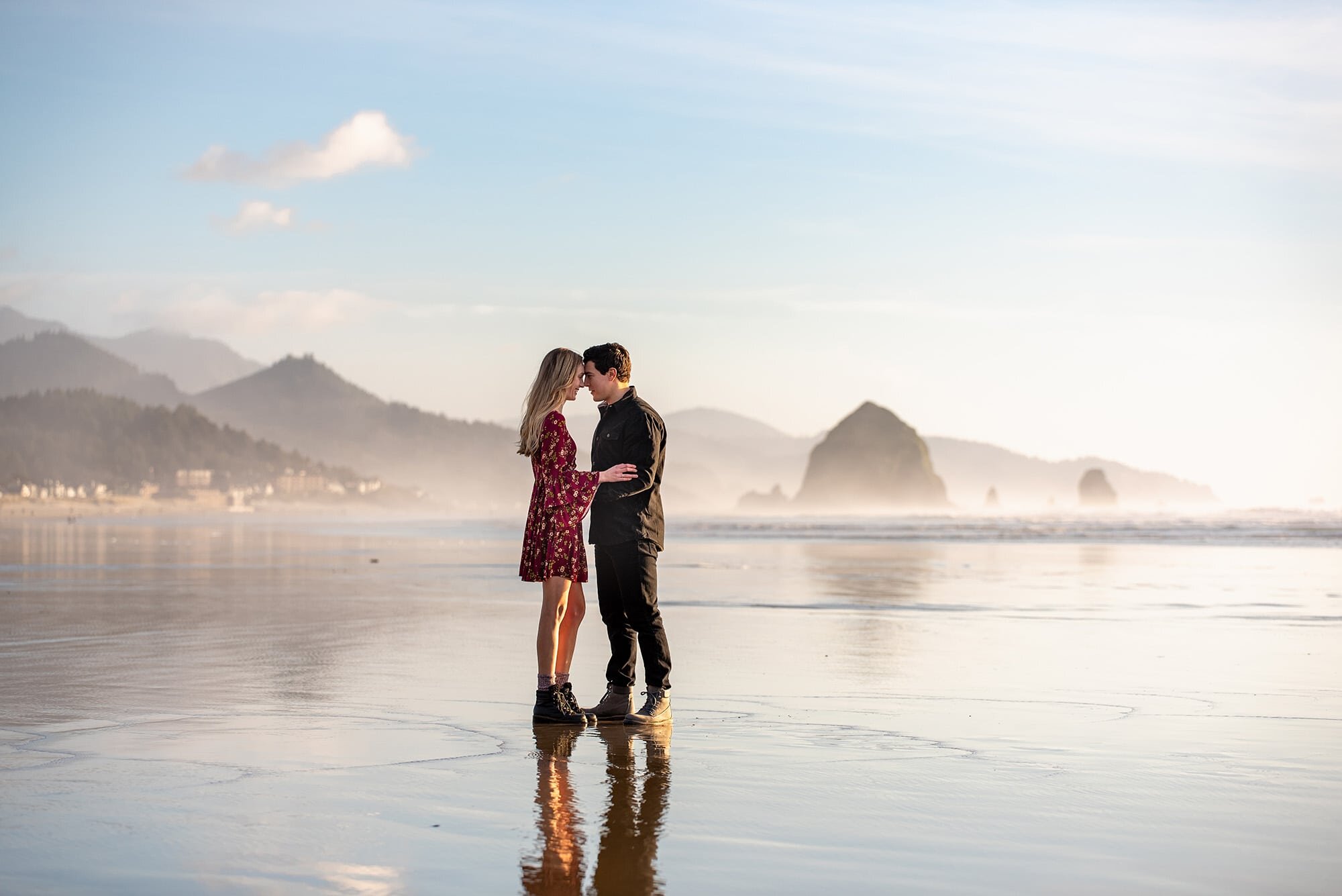 Engaged couple standing on reflective sand at Cannon Beach